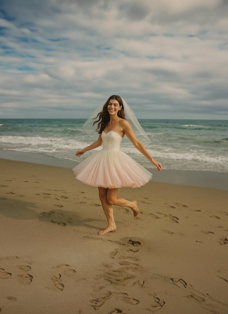 Wide shot of a model wearing a blush ombre mini wedding dress on a beach at sunset.