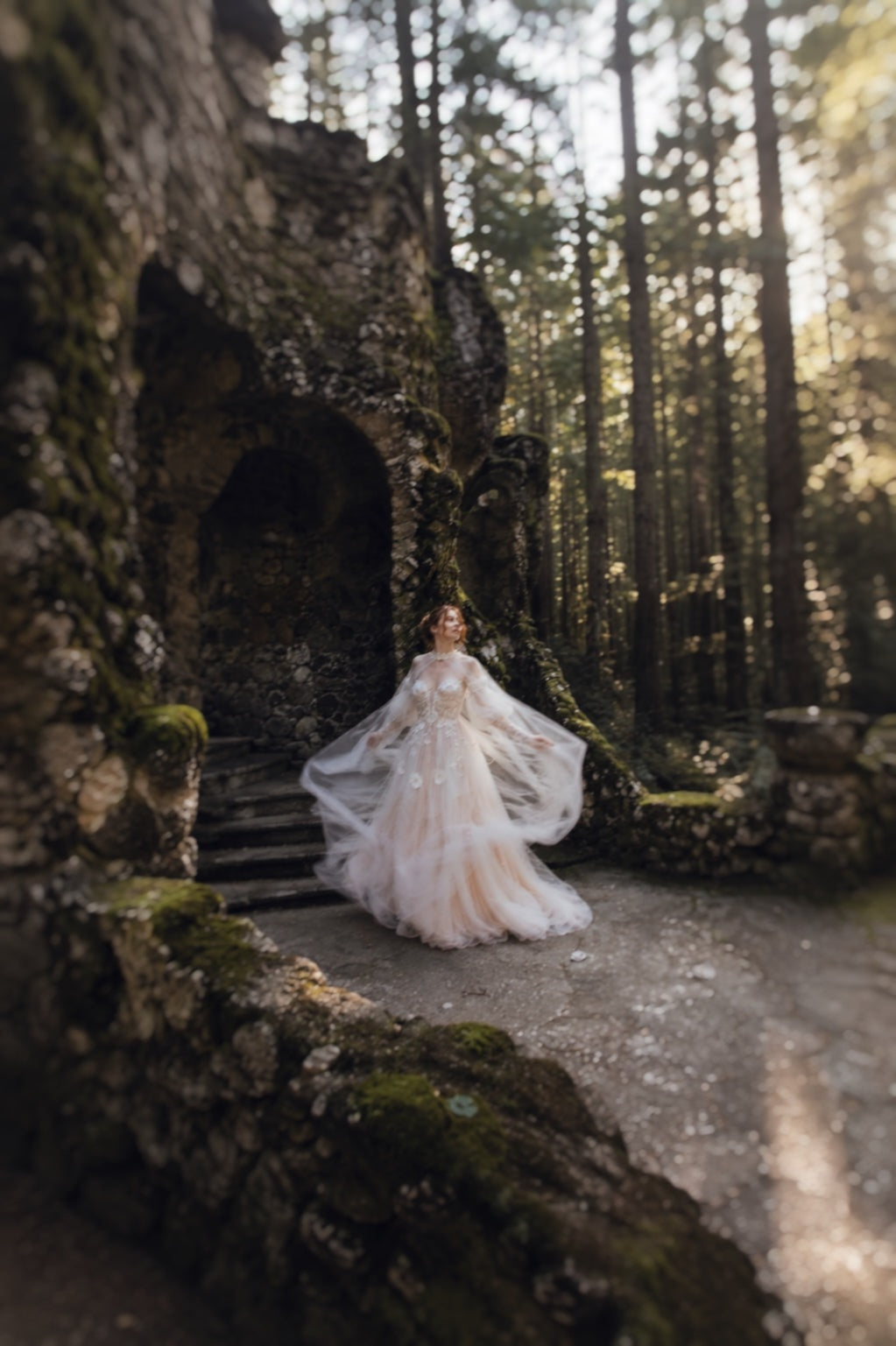 Full-length Arrowyn ethereal wedding dress with flowing cape in woodland ruins.