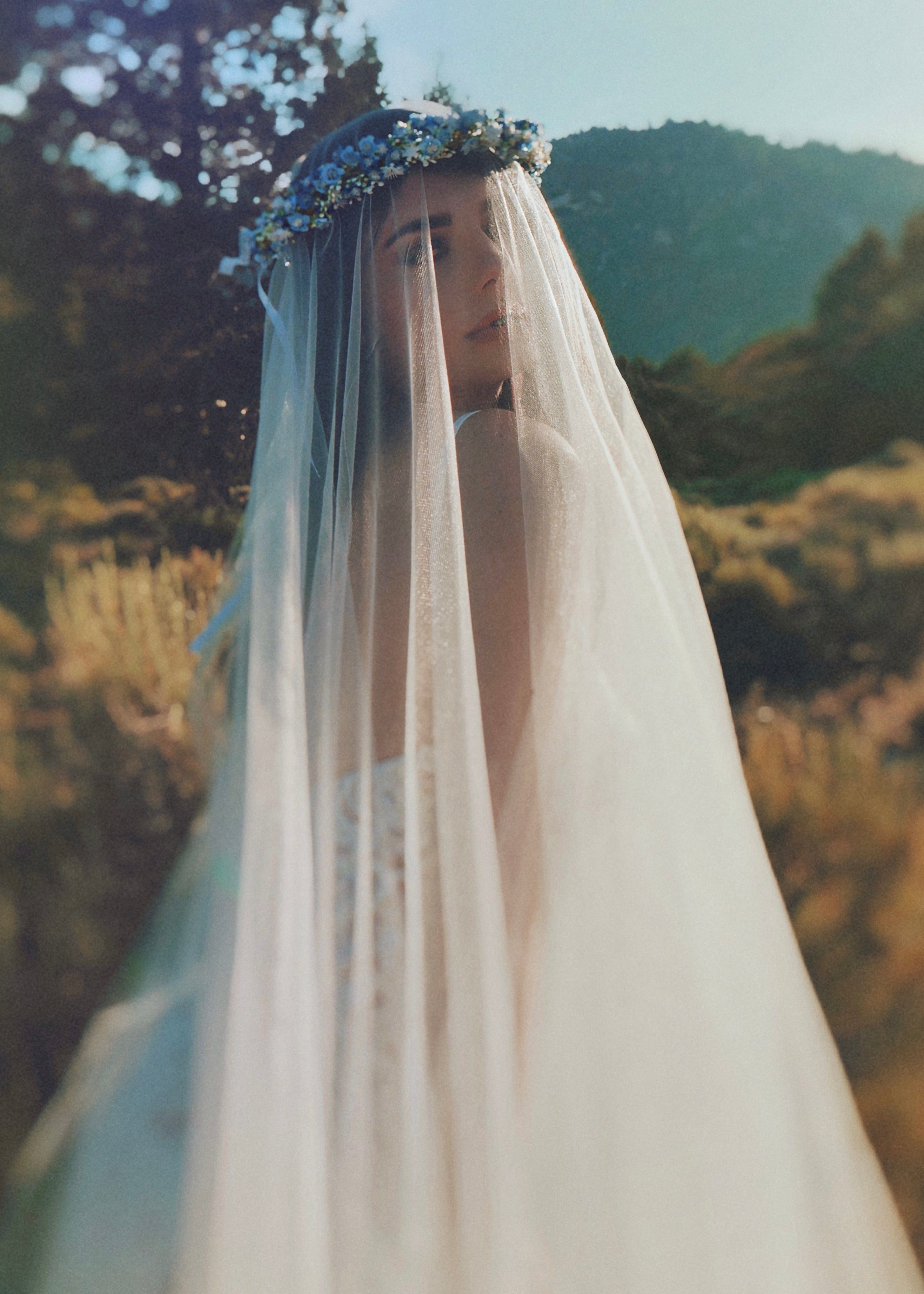 A woman wearing a natural white tulle blusher wedding veil with a silver hair comb, from the 'Wildbloom' collection.