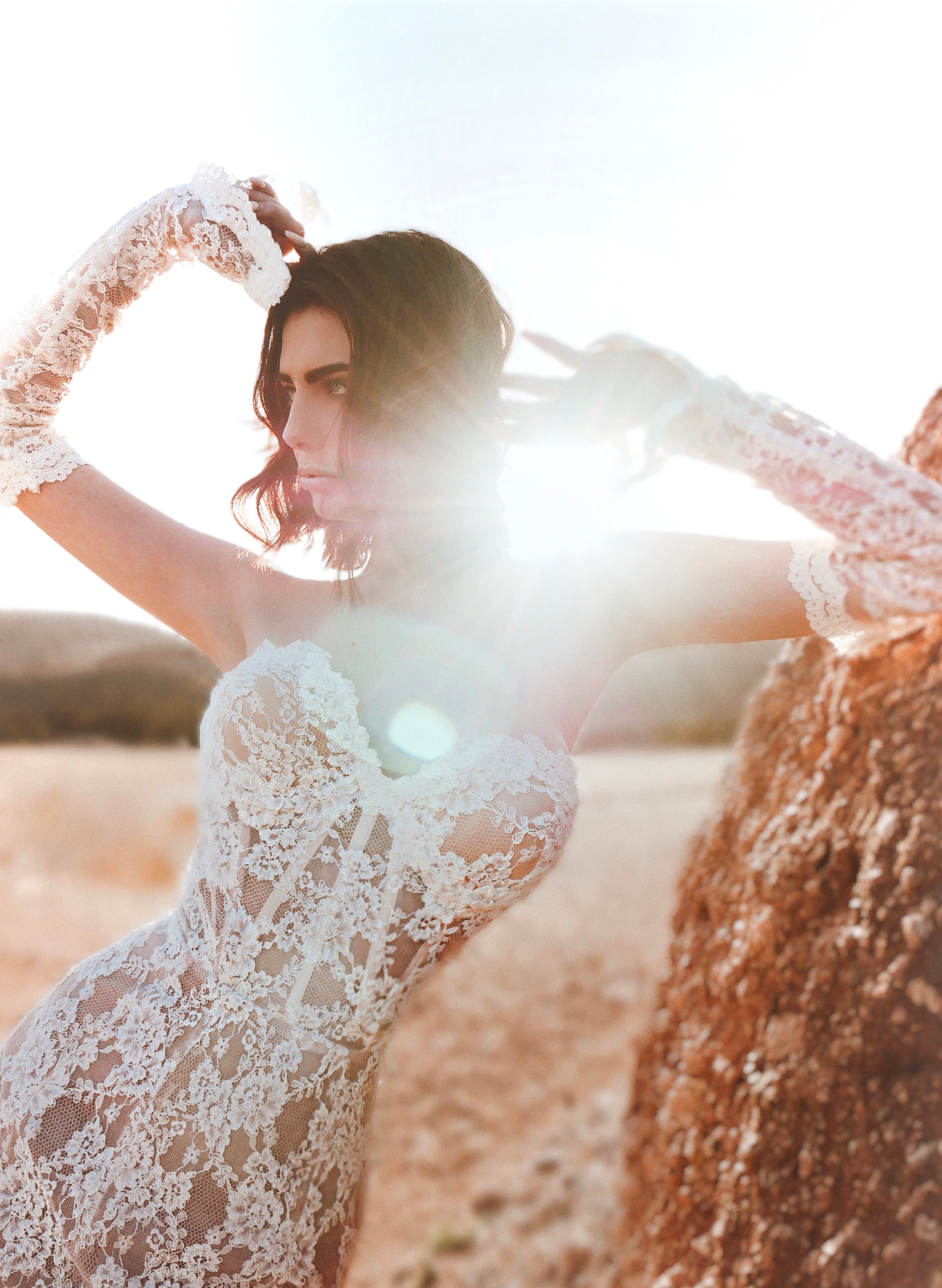 A model poses in alencon lace bridal glove sleeves against a desert backdrop at golden hour.