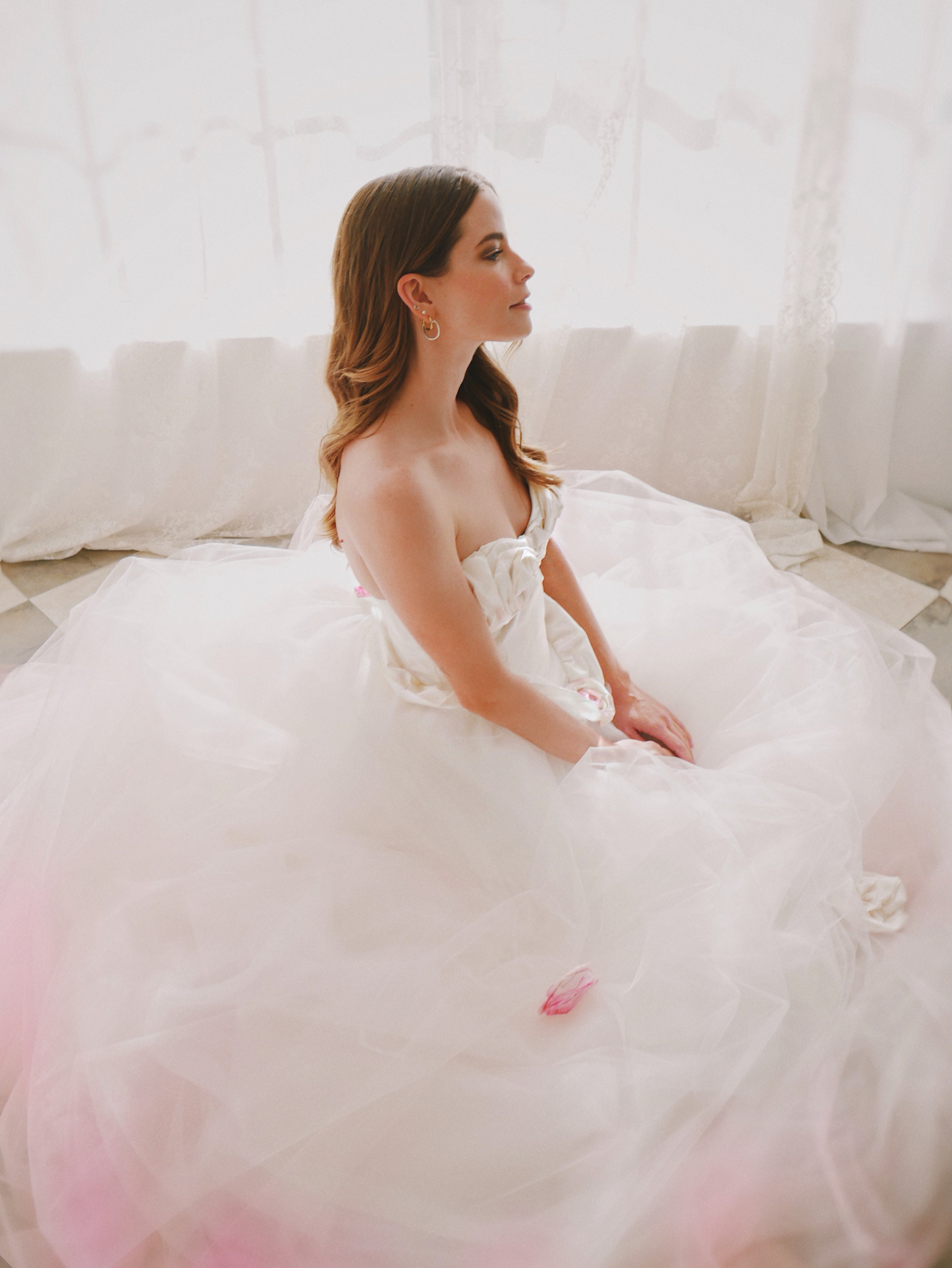 A model sits in the Lauren Elaine "Duchess" Blush Pink Wedding Dress with Rosettes