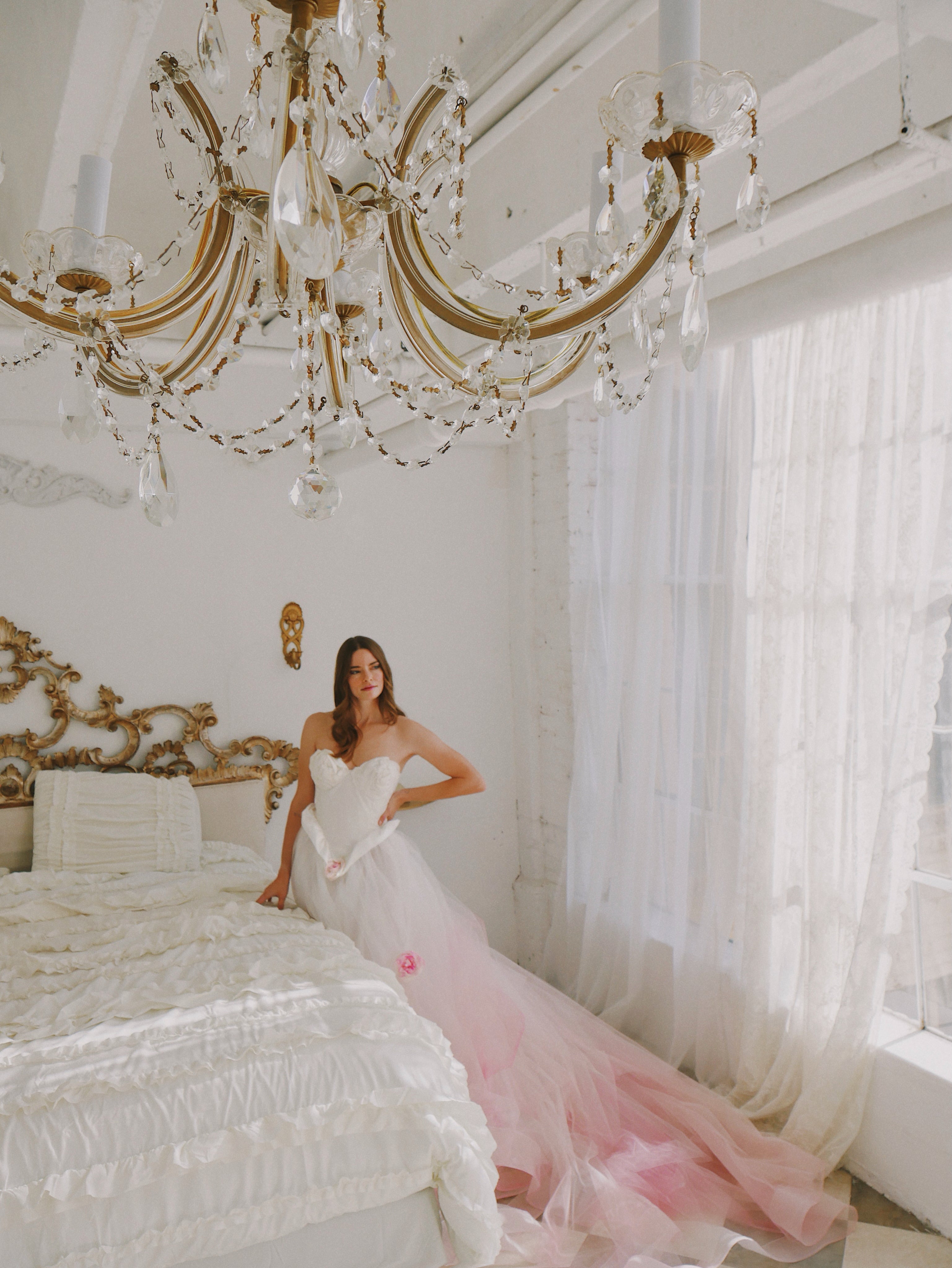 Bride sitting on bed in mansion wearing ombre tulle pink wedding gown