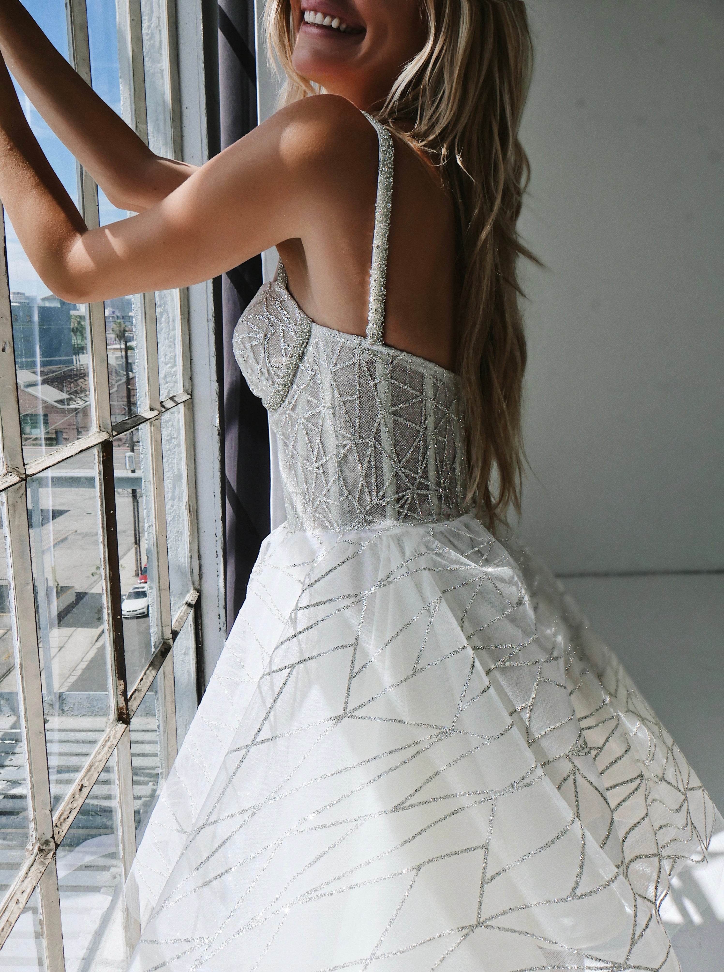 A model wears a sparkling mini wedding dress at photo studio in front of a window.