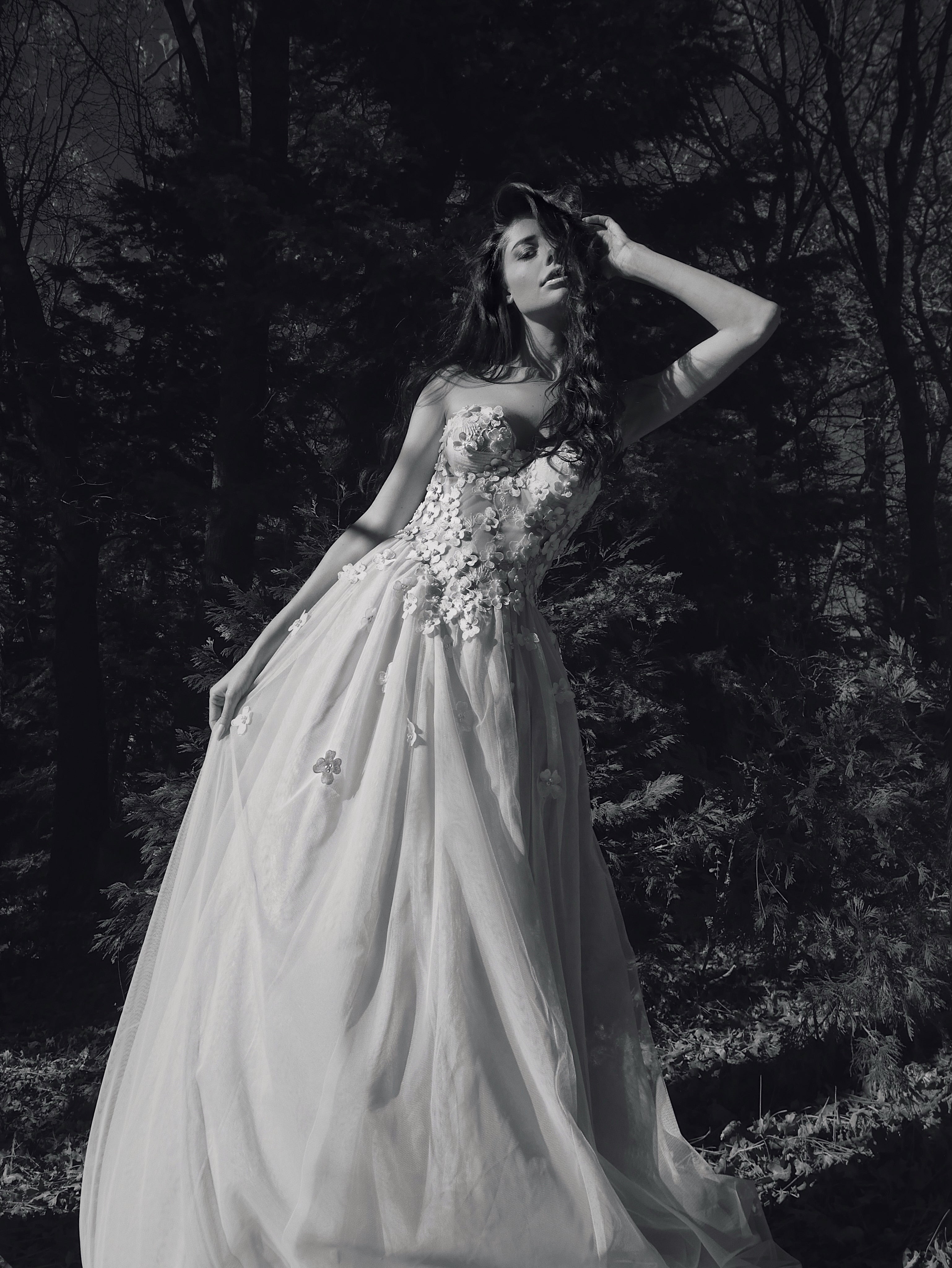 Valen ethereal bridal gown with floral lace bodice, flowing tulle skirt, and detachable sleeves photographed in a dramatic woodland setting