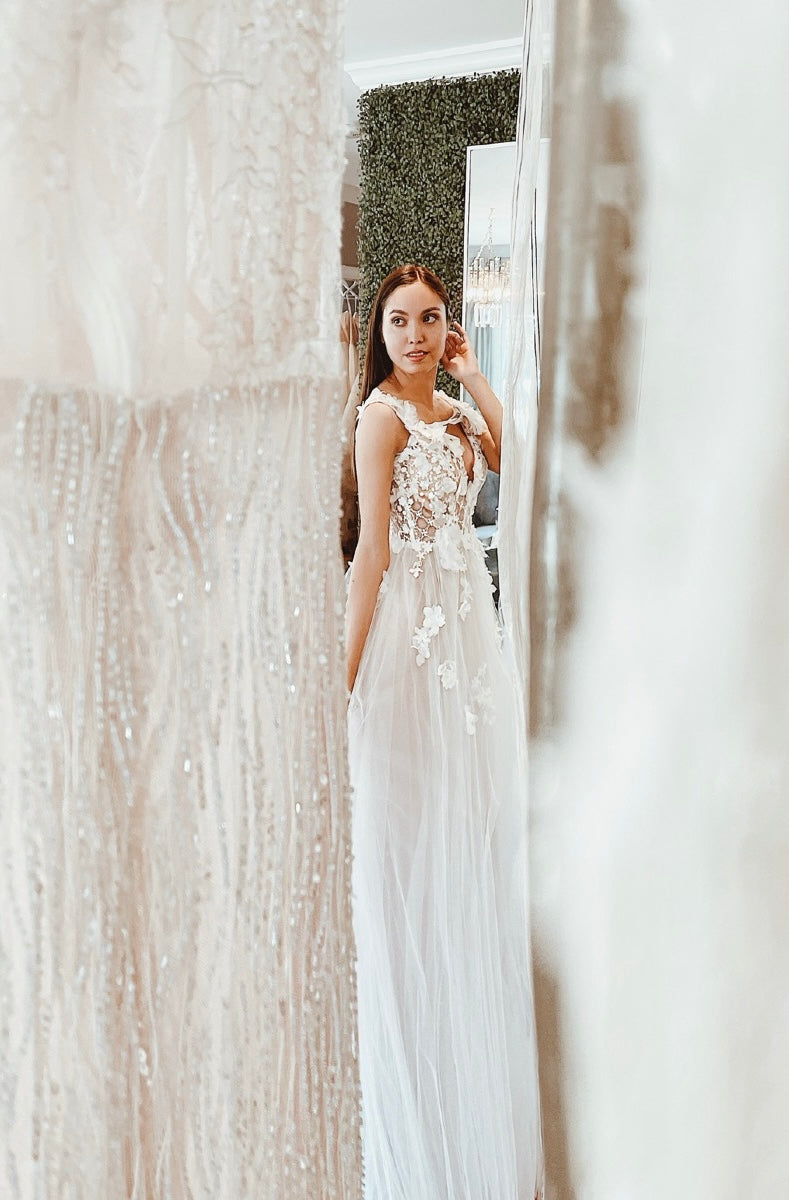Bride standing between wedding dresses in Lauren Elaine Bridal Los Angeles studio