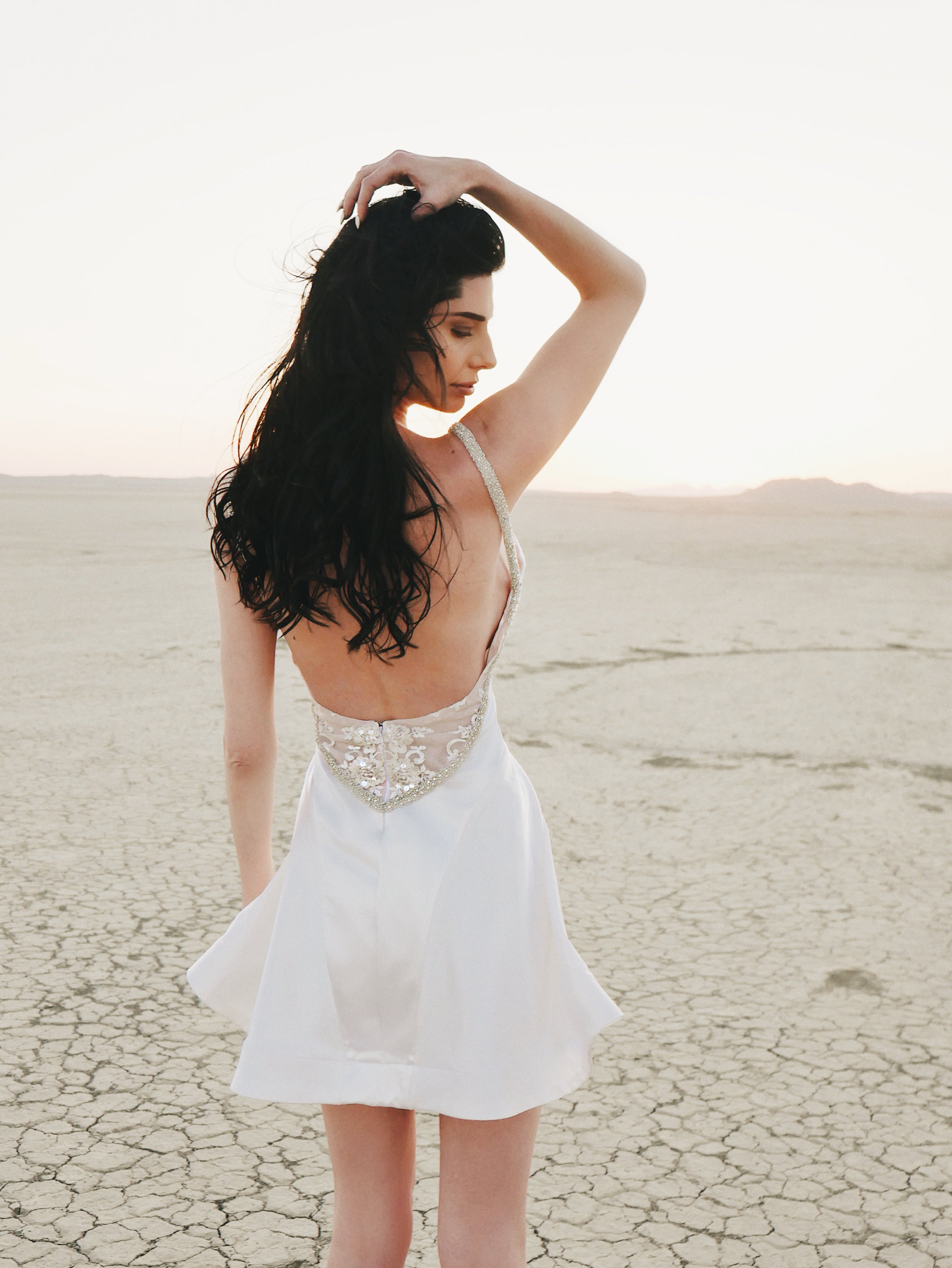 Lauren Elaine Affinity Backless Satin Mini Wedding Dress with crystals on a model in the desert.