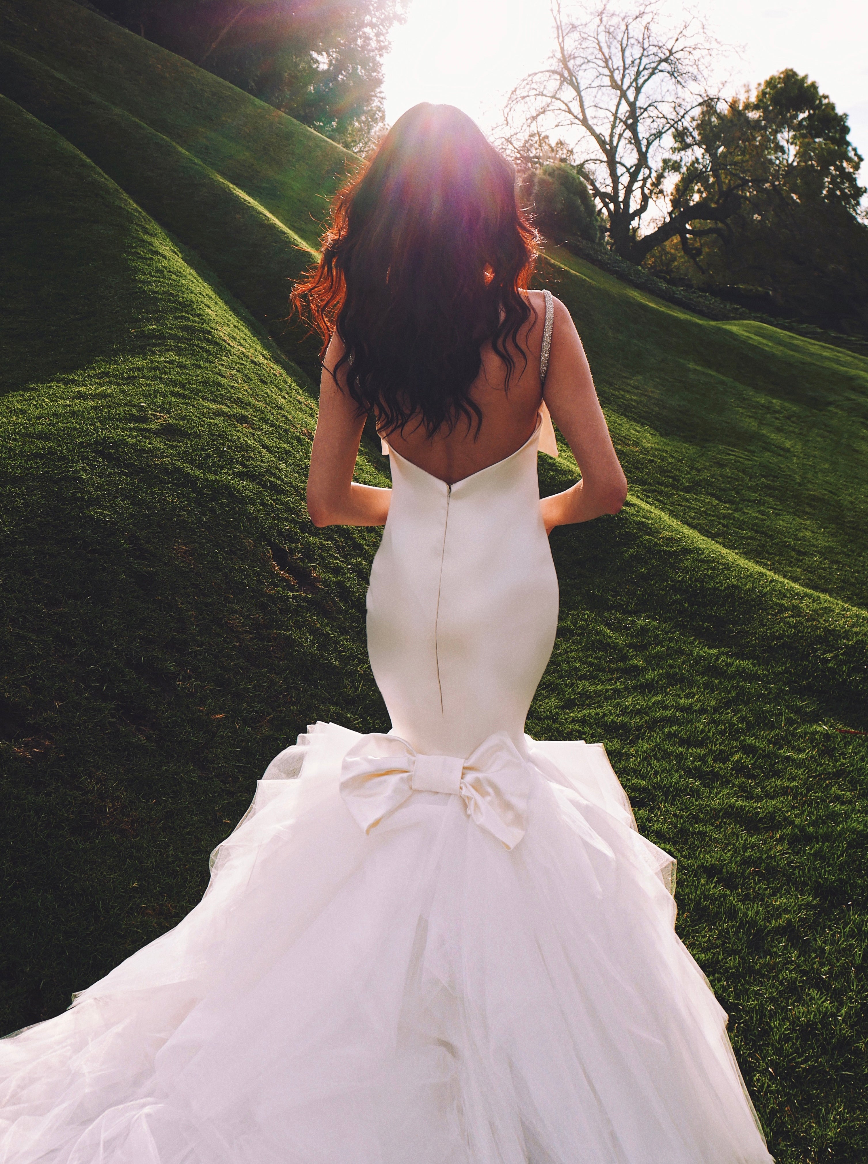 Back of satin wedding gown with bow on model on grass