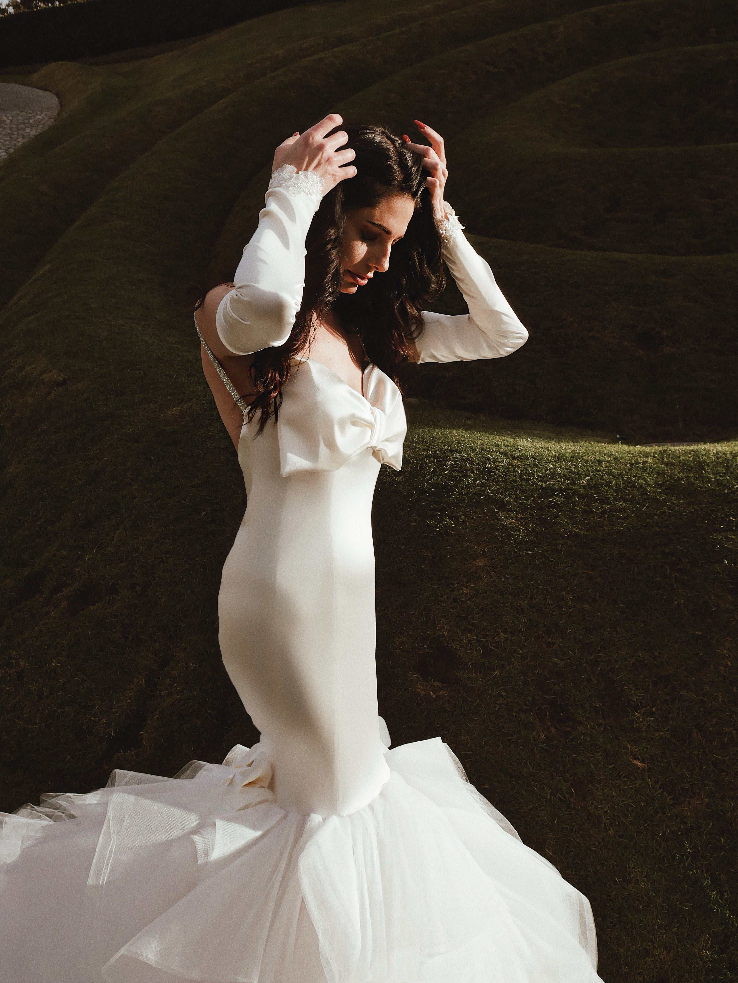 A bride wears sleek satin glove bridal sleeves paired with a satin mermaid wedding dress with bow.