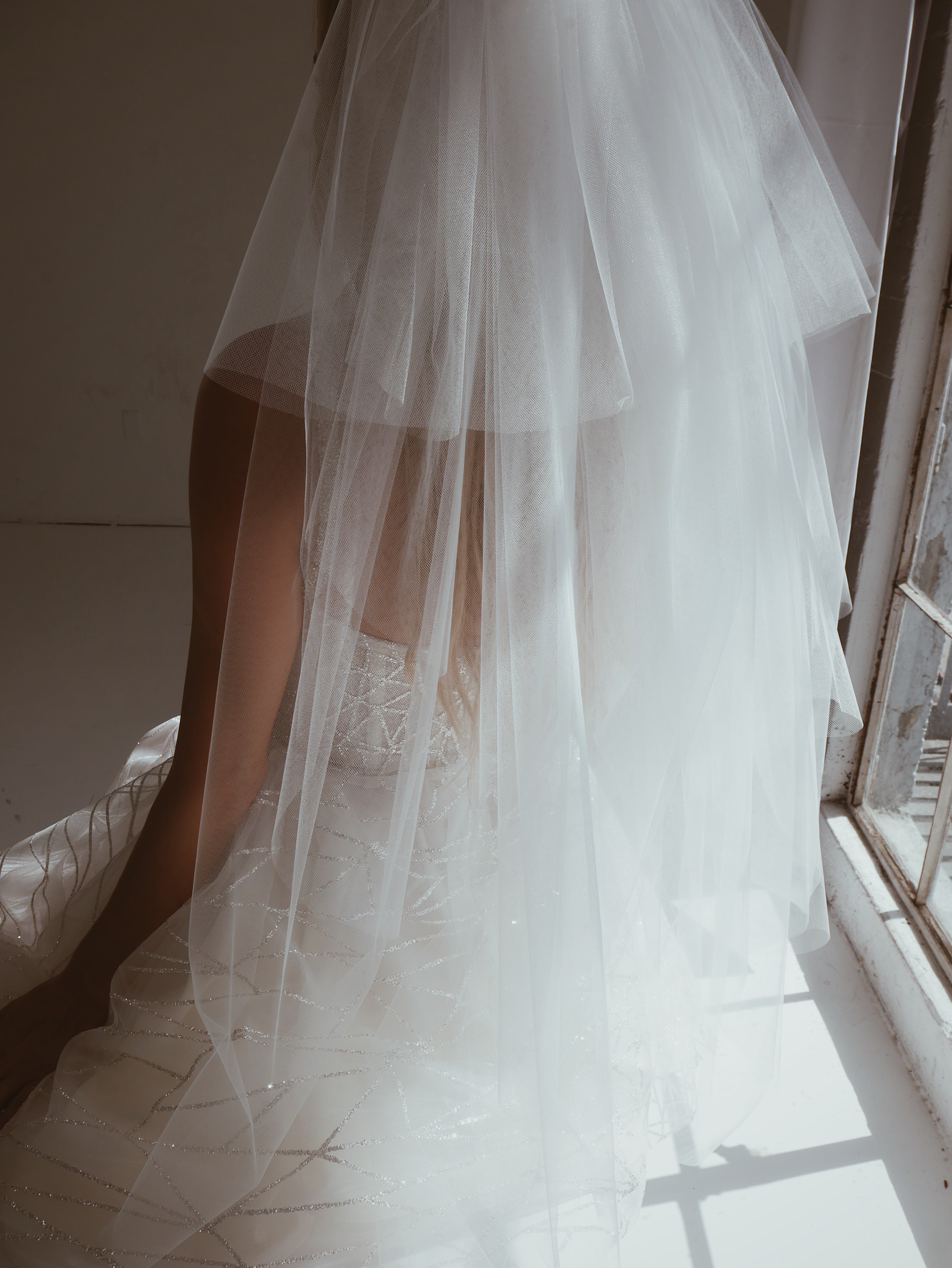 Back view of a model wearing a statement tiered tulle wedding veil with crystal comb in 1980s style.