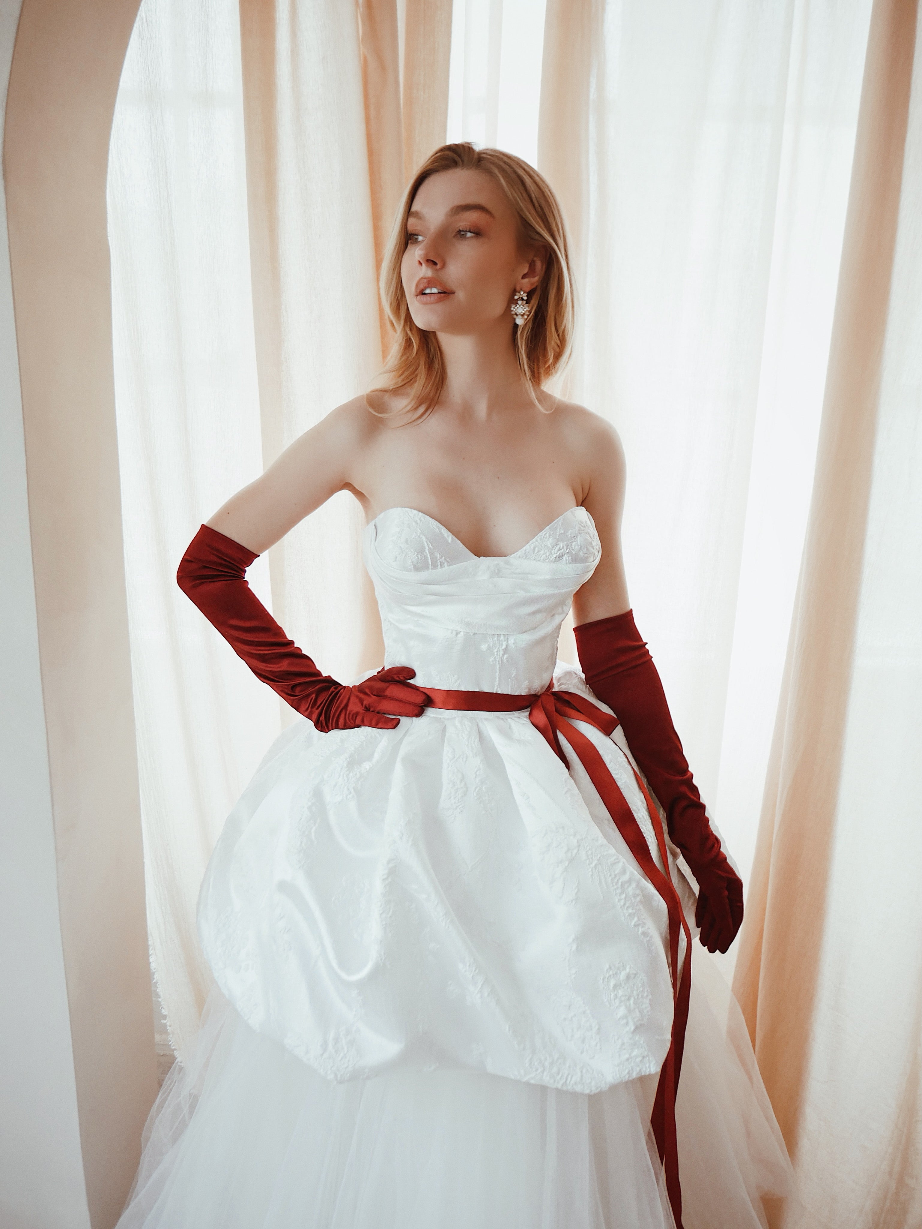Detail photo of a model wearing a satin corset wedding dress w/ red opera gloves and ribbon sash.