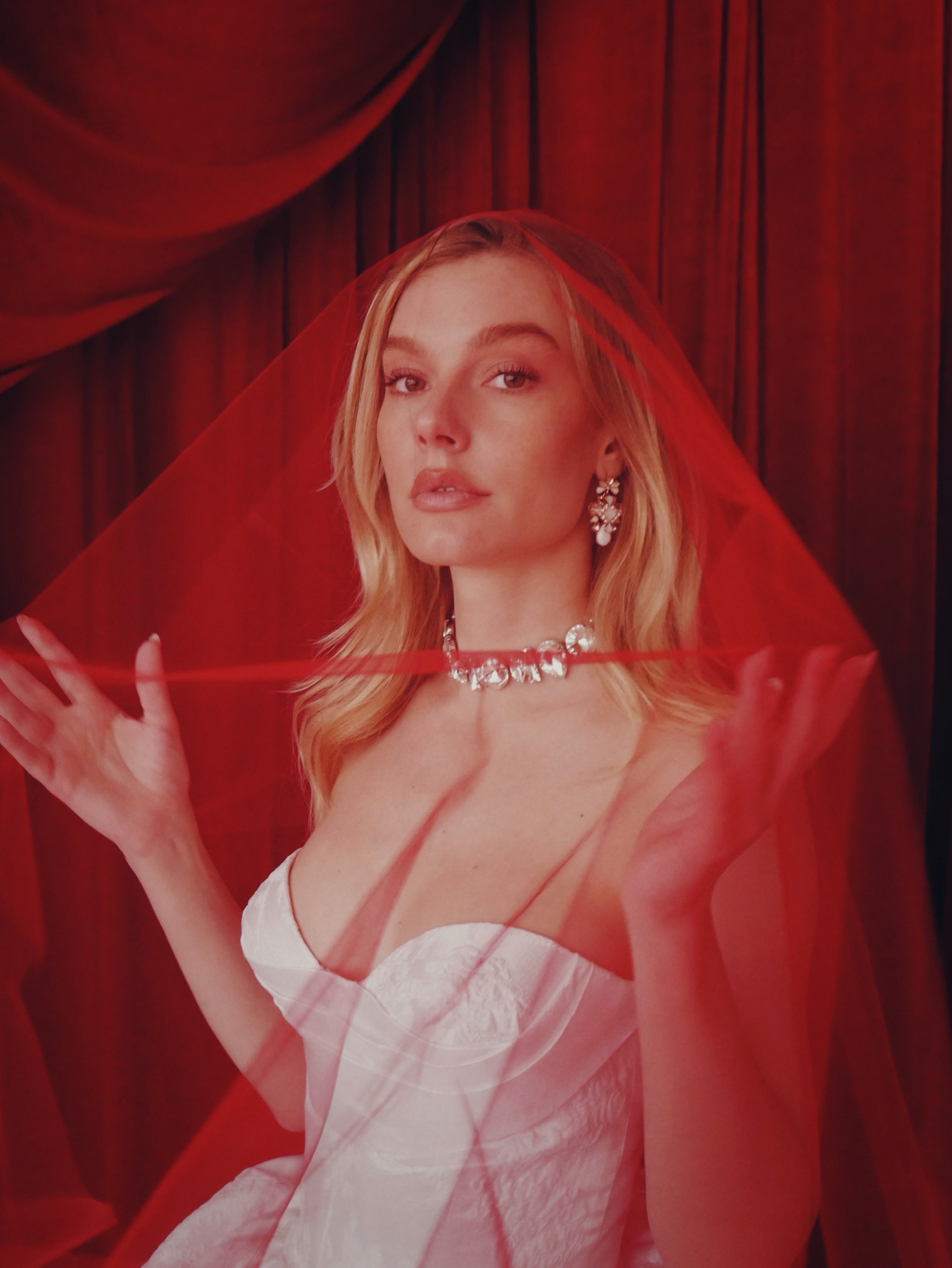 Close up image of a model posing in a red wedding veil and corset sweetheart wedding dress.