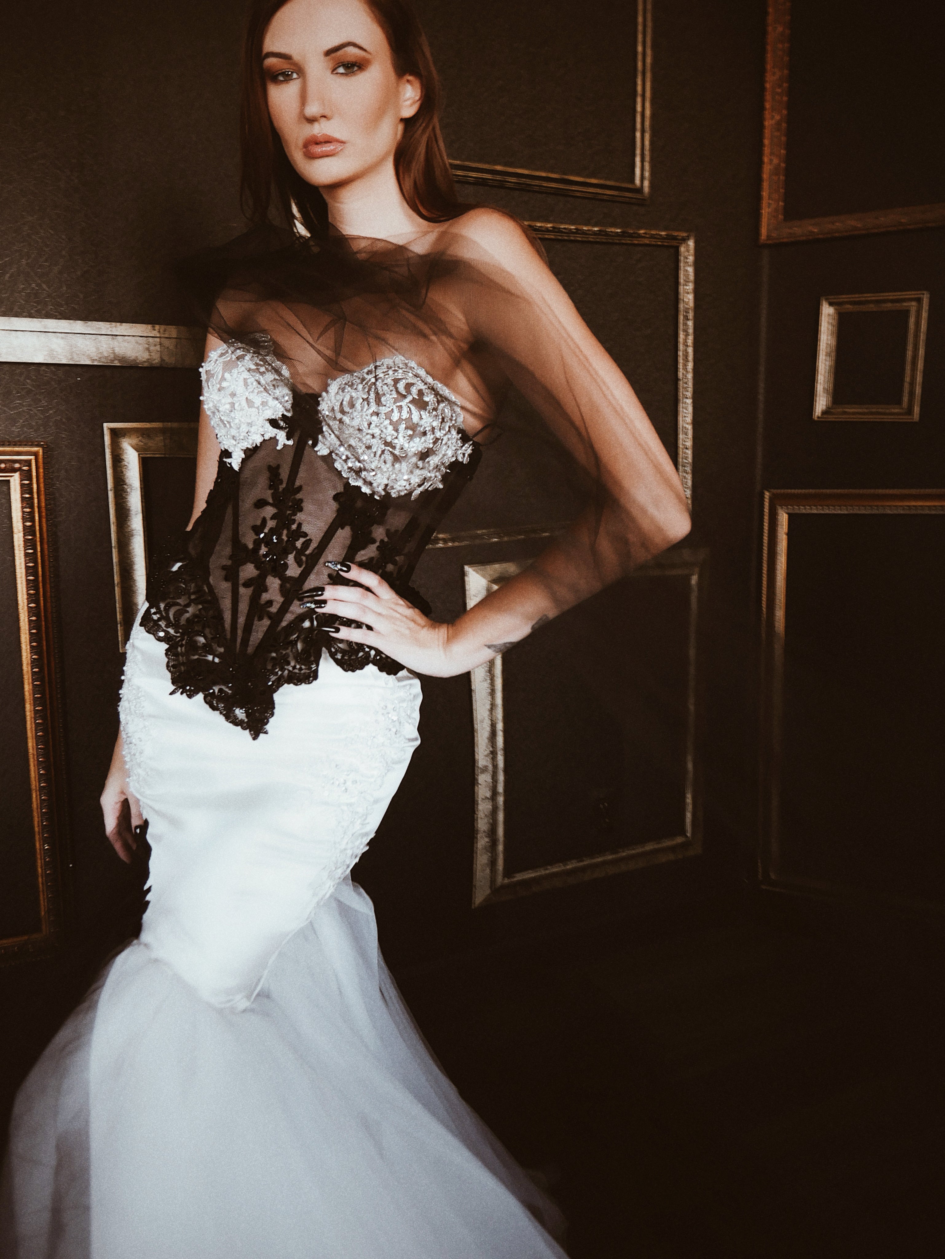 A model poses in a black and white Basque waist corset mermaid wedding dress with satin hips.