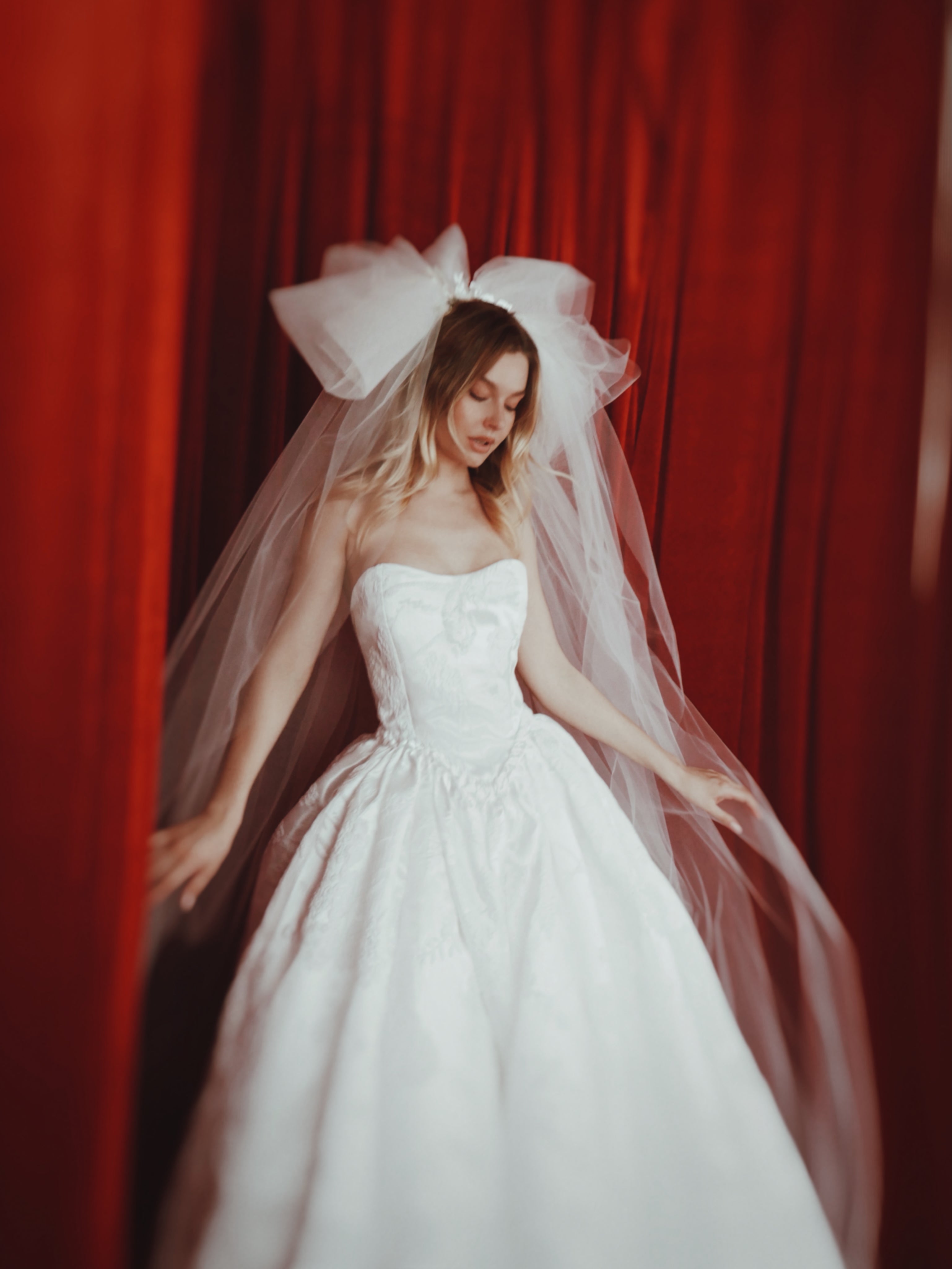 A model poses in a dramatic vintage inspired layered tulle wedding veil and satin wedding dress.
