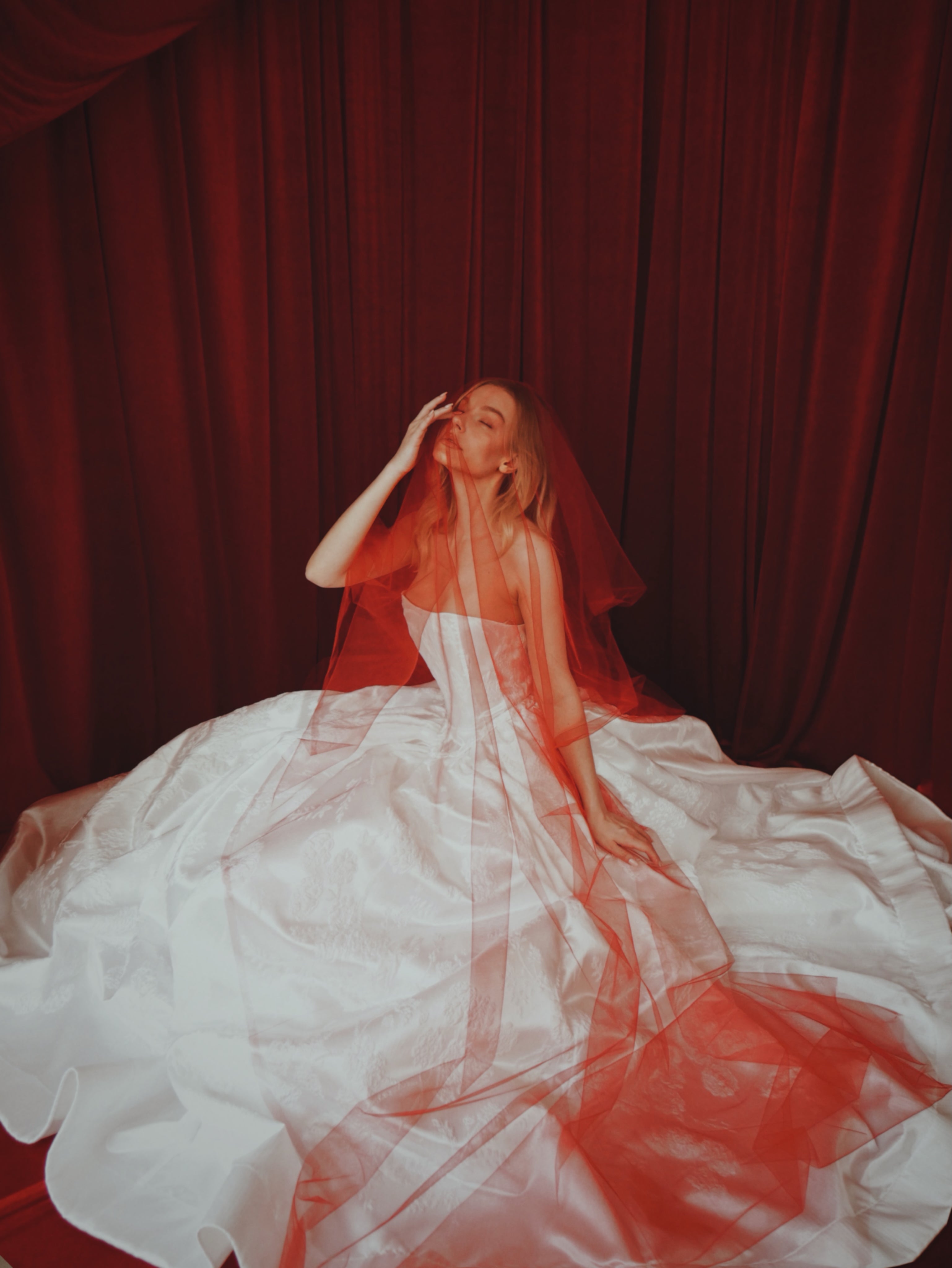 A model poses in a  satin brocade basque waist corset wedding dress with red veil.