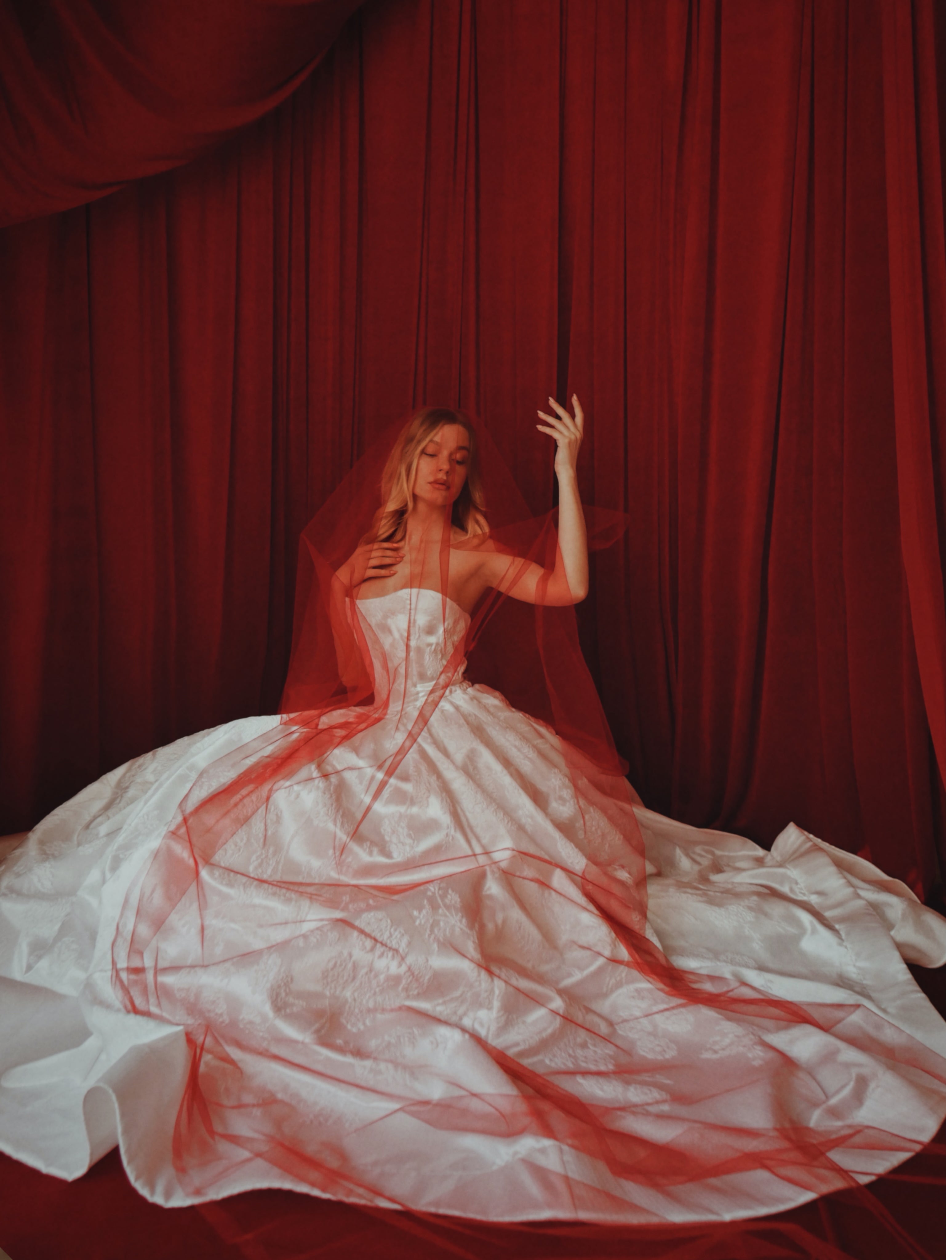 A model sits in a  satin brocade basque waist corset wedding dress with red veil.