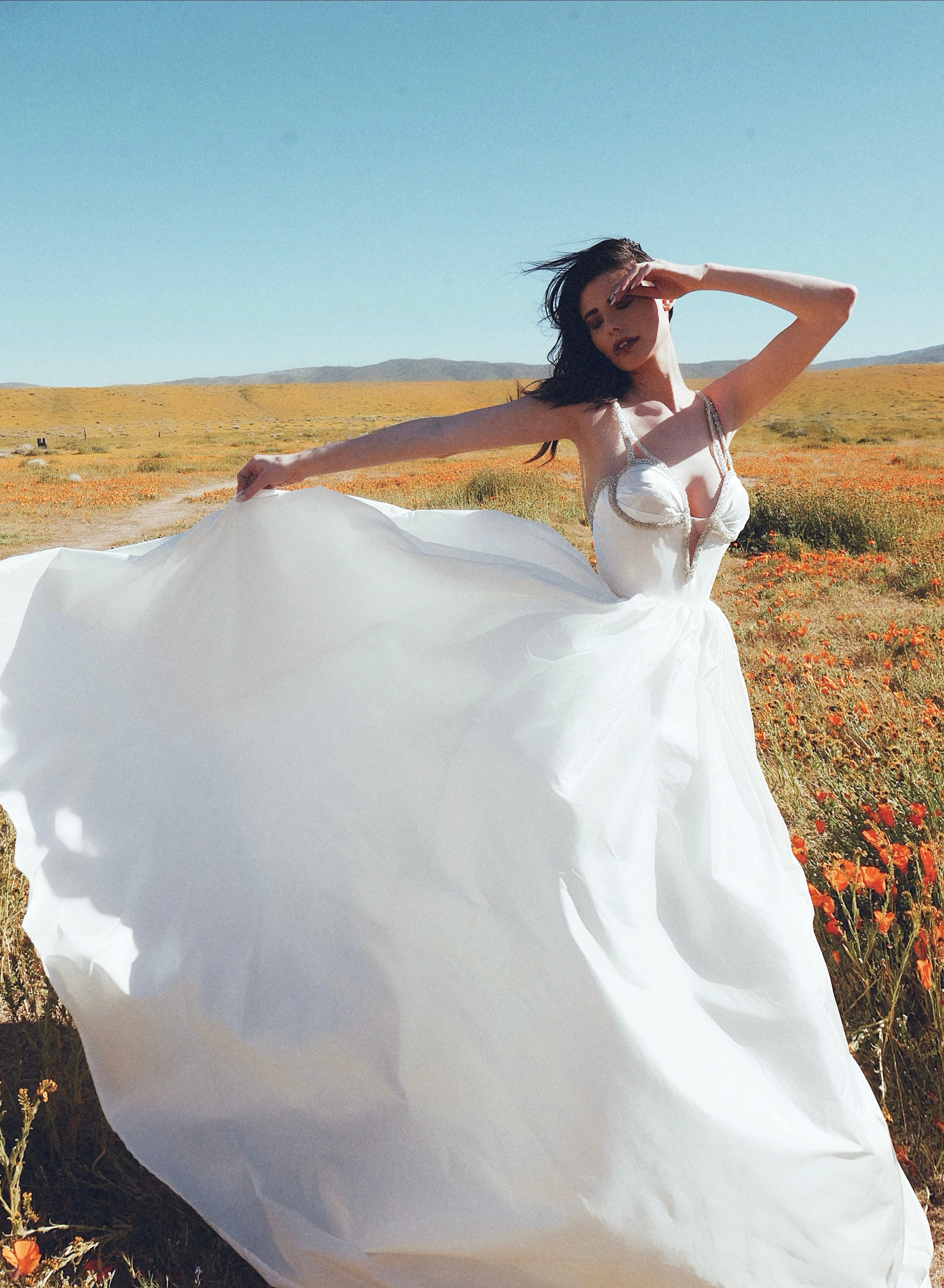 A model wears the Lauren Elaine Vespertine silk taffeta corset wedding dress in a field of poppies.