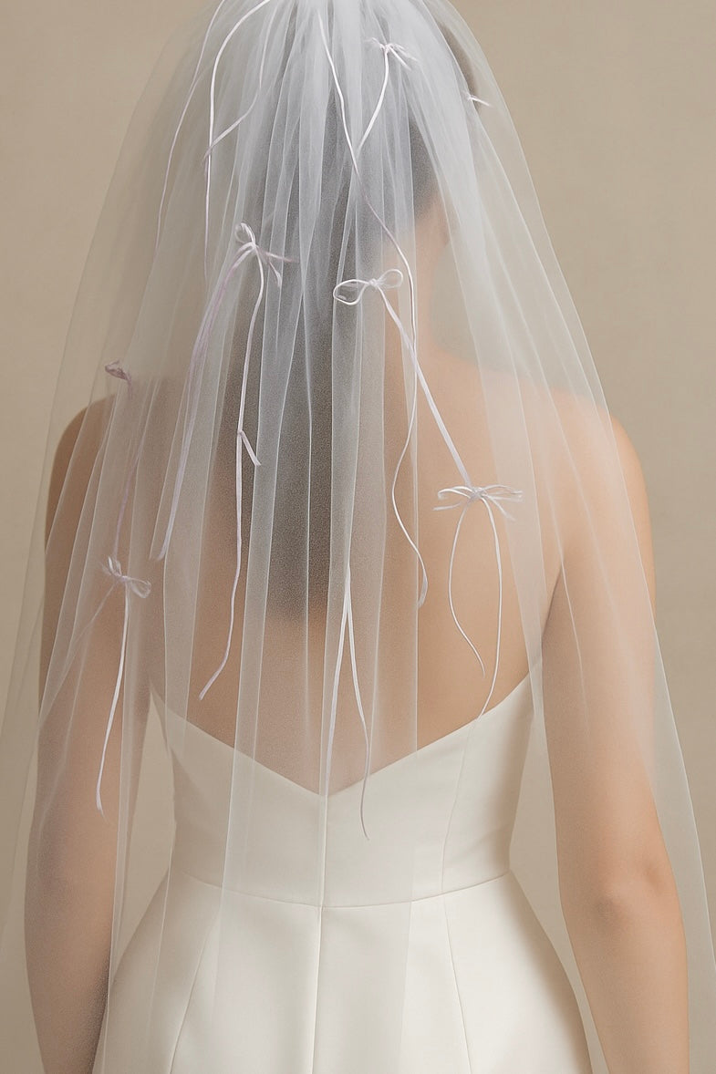 A bride wears a veil covered in tiny bows in shades of ivory and white.