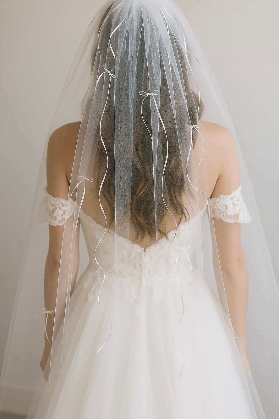 A bride wears a wedding veil with mini satin bows in shades of ivory.
