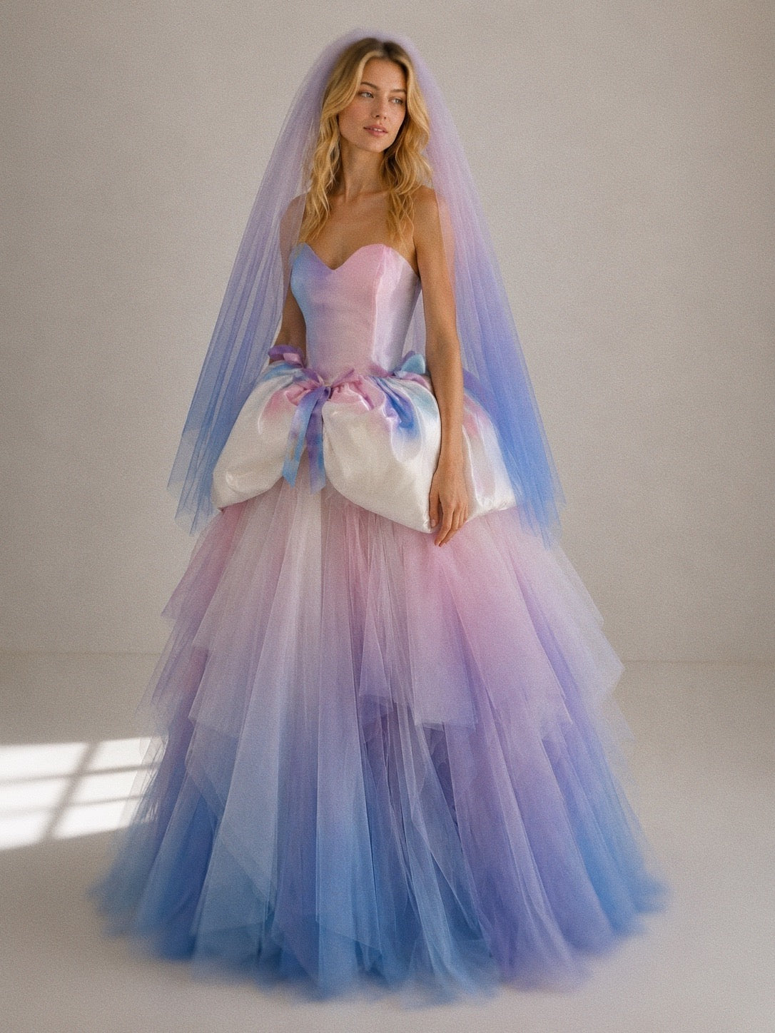 Moondreamer rainbow wedding dress by Lauren Elaine featuring a watercolor satin sweetheart basque waist bodice, balloon peplum, pastel ombré tulle ball gown skirt, and matching rainbow veil.
