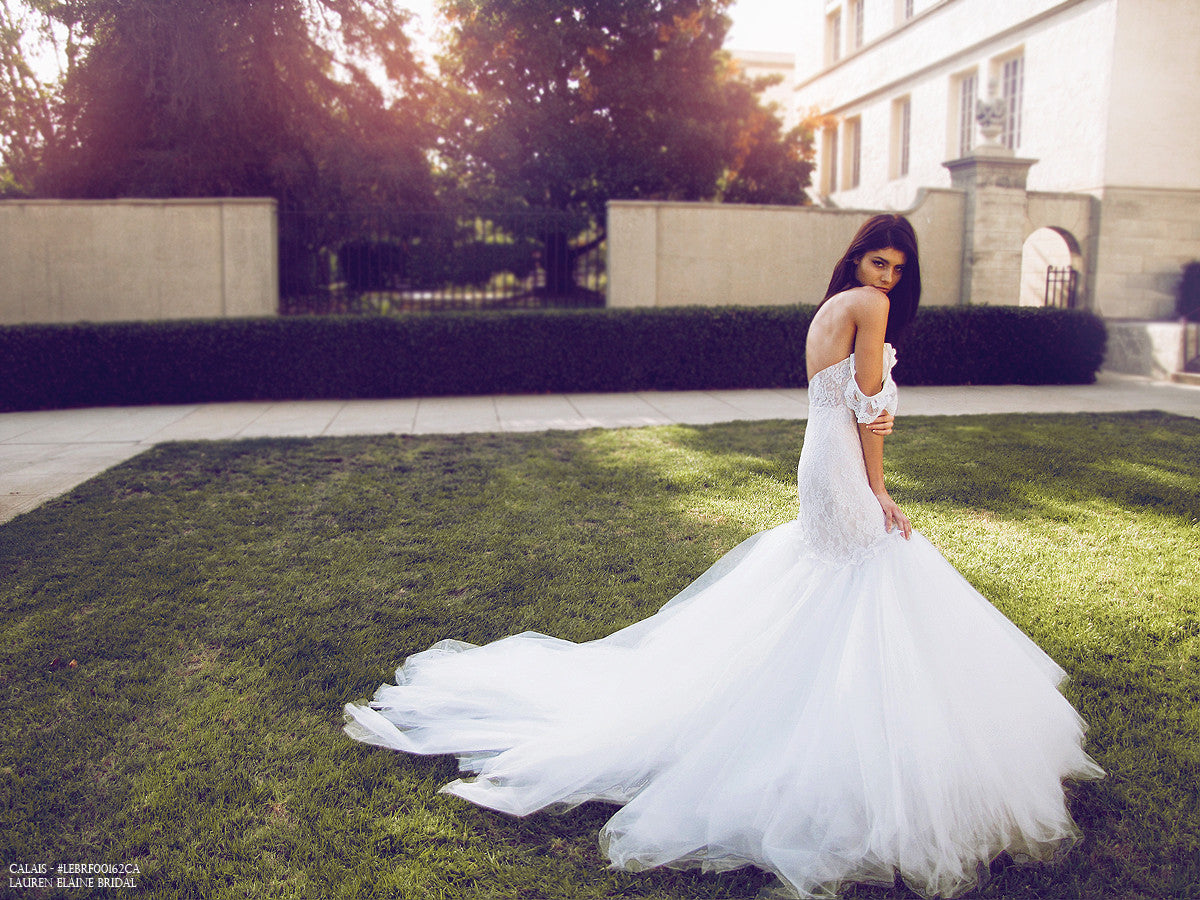 Dramatic mermaid wedding dress with cathedral train and off-the-shoulder lace sleeves.