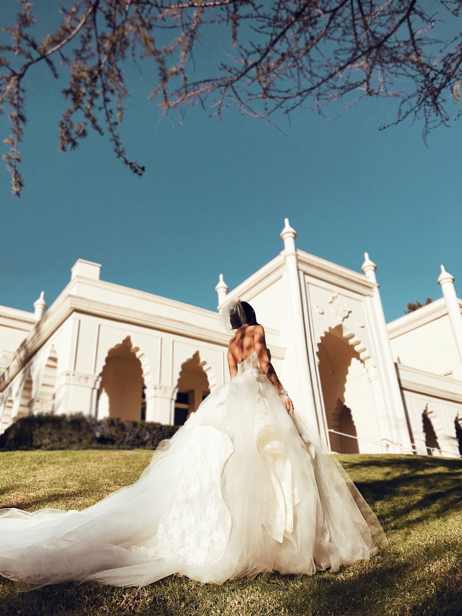 A model wears a tulle ball gown wedding dress with dramatic detachable cathedral train.