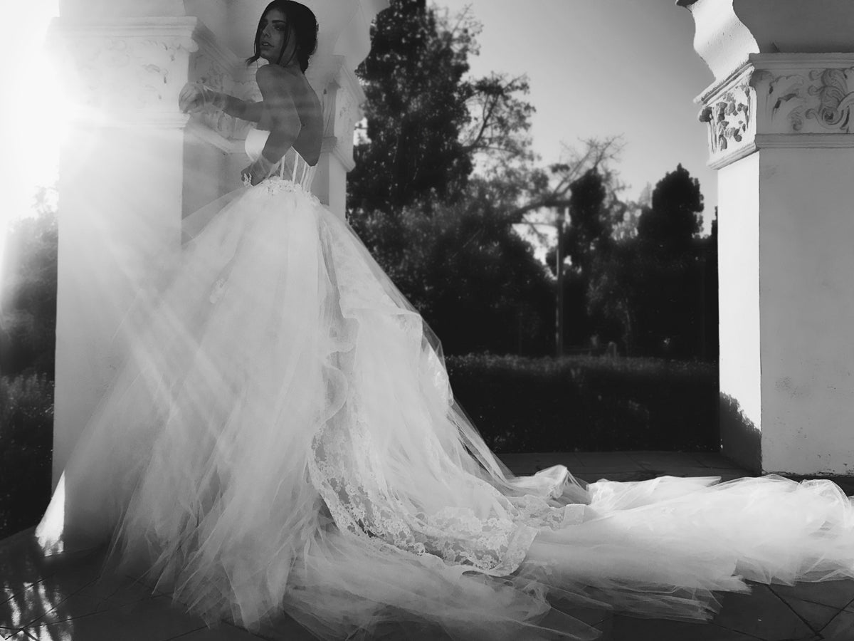Side view - A model wears a tulle ball gown wedding dress with dramatic detachable cathedral train.
