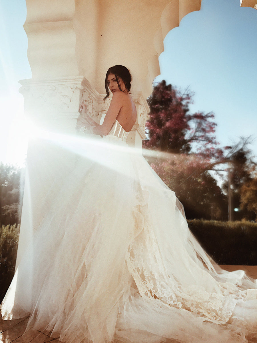 A model wears a tulle ball gown wedding dress with dramatic detachable cathedral train - side view.