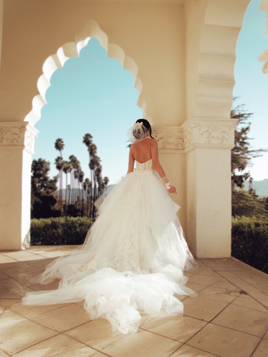 Back view - A model wears a tulle ball gown wedding dress with dramatic detachable cathedral train.