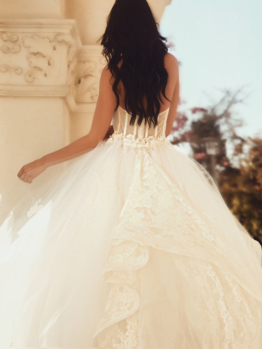 Back view closeup of A model wears a tulle ball gown wedding dress with dramatic cathedral train.