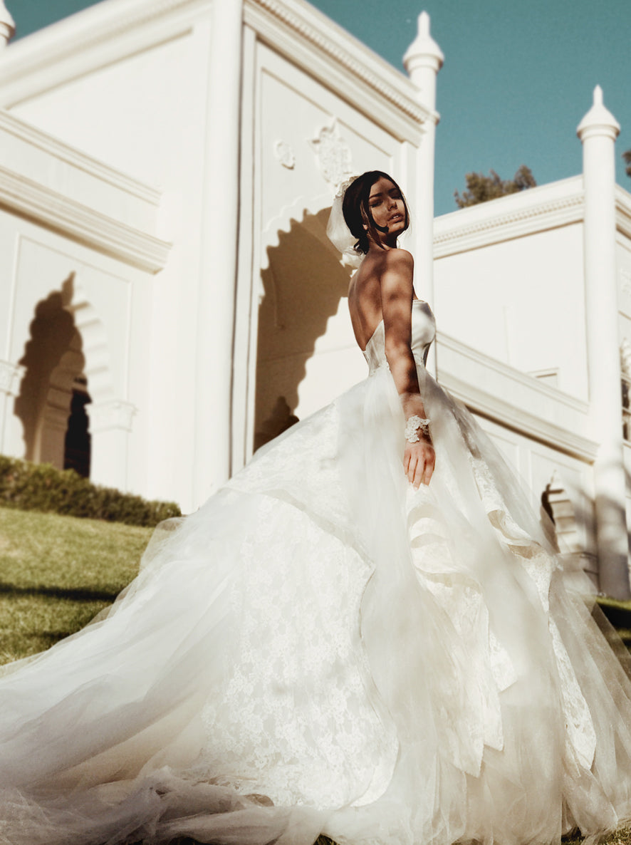 A model wears a tulle ball gown wedding dress with dramatic detachable cathedral train - side view.