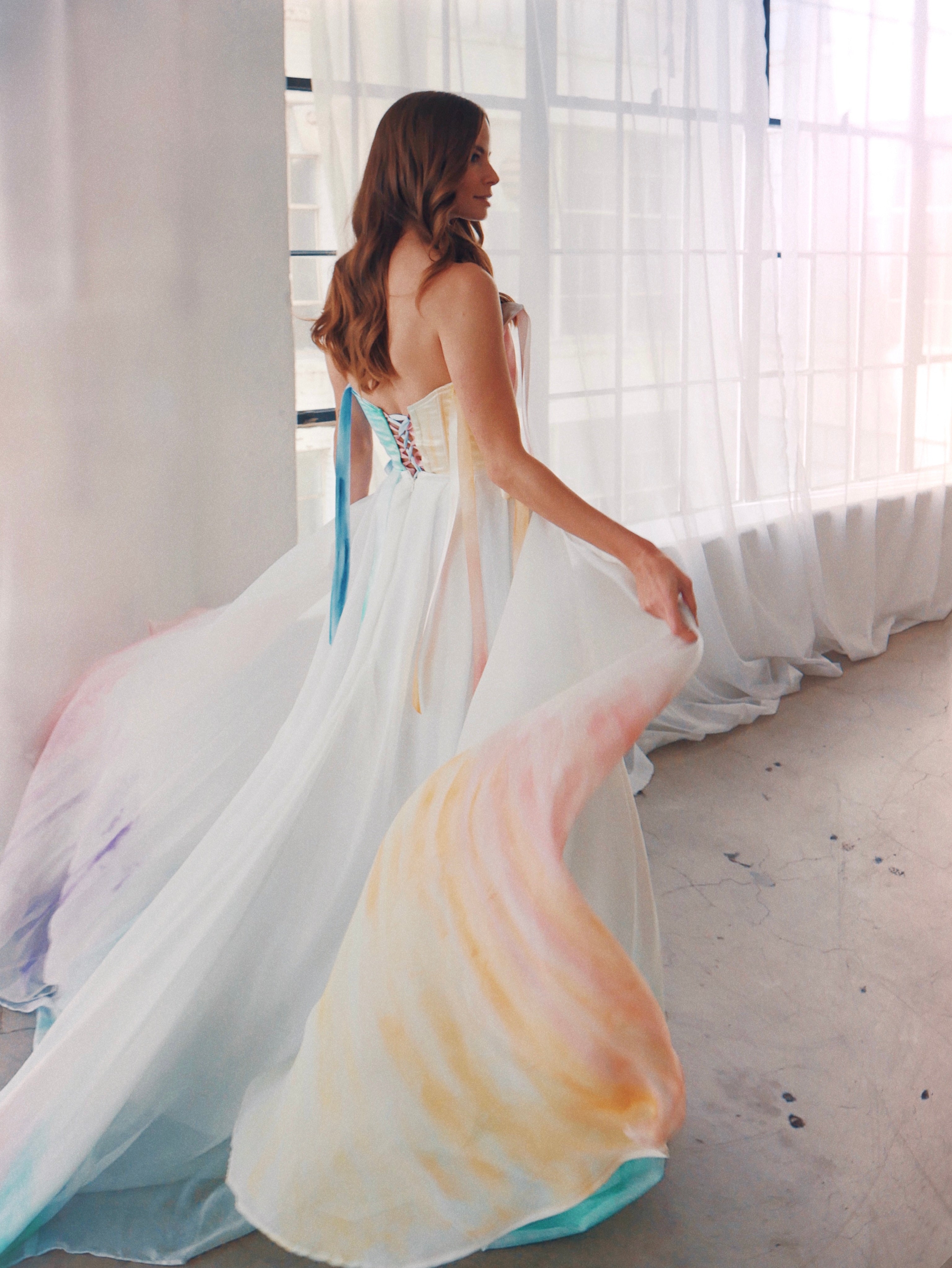 Bohemian rainbow wedding dress in motion with flowing ombré chiffon skirt and corset bodice, light-filled studio setting