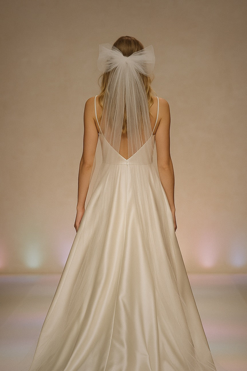 A model wears an oversized tulle bow wedding veil on a runway.