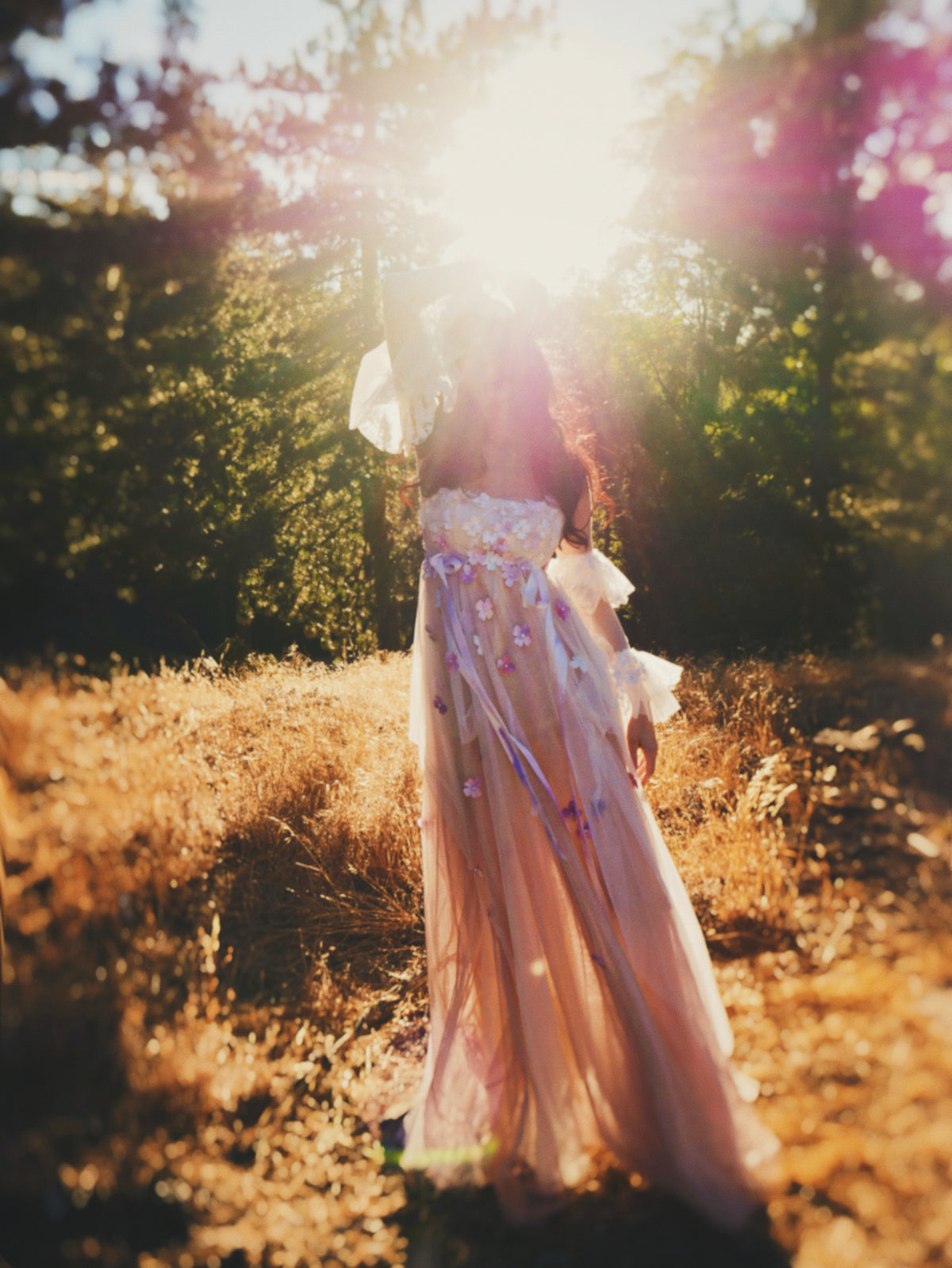 Full-length Florêve colorful floral wedding dress with pink and lavender wildflowers in a sunlit woodland
