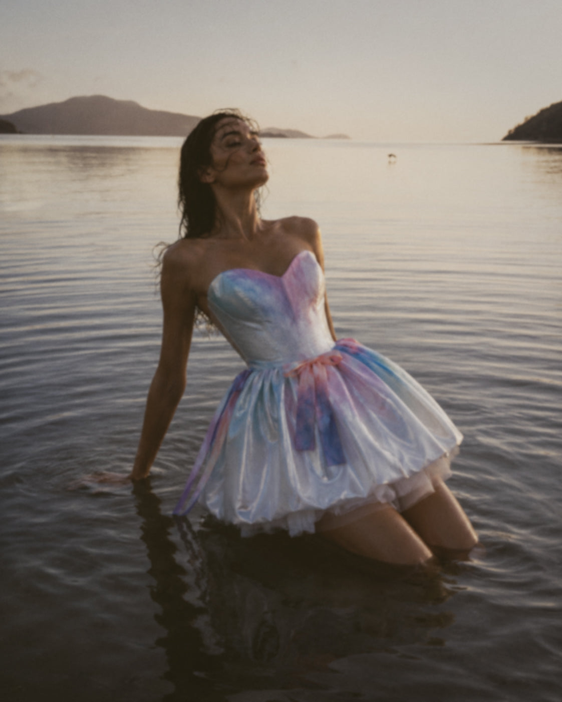 Colorful bridal mini dress with pastel rainbow watercolor satin and cathedral veil photographed on a rocky beach at twilight