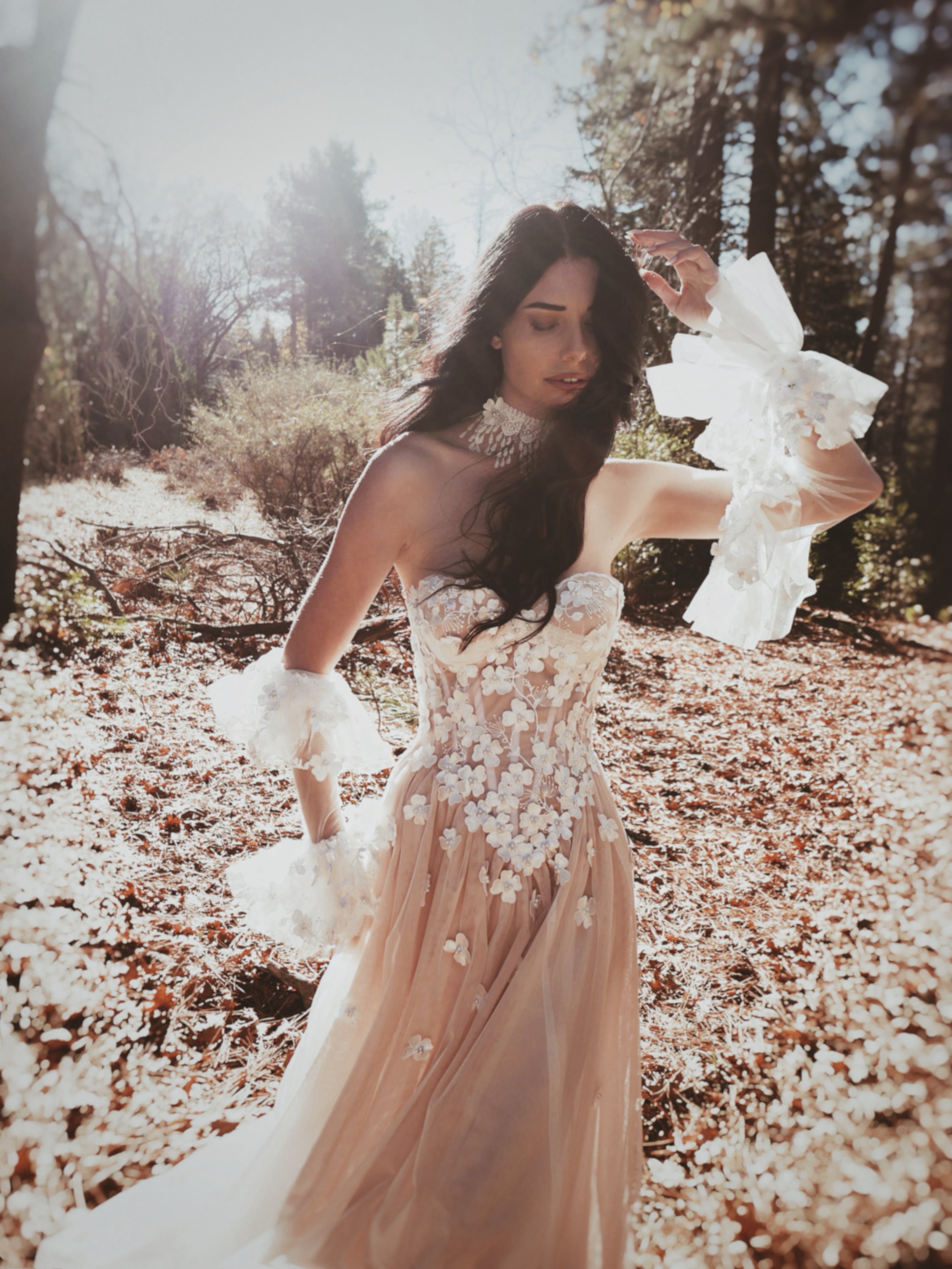 Valen bohemian A-line wedding dress with basque waist, exposed corset bodice, and dimensional floral appliqués in a romantic forest setting