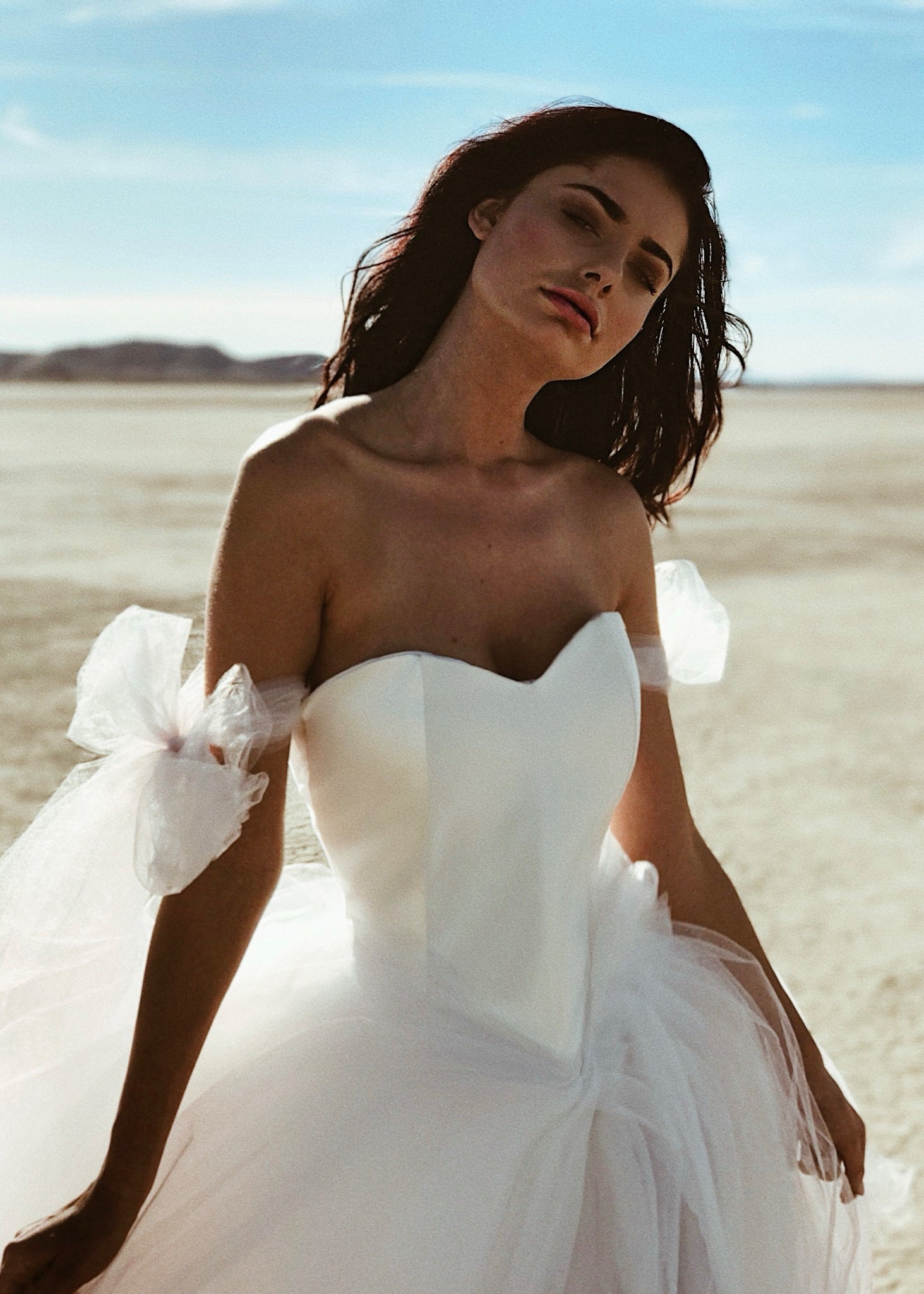 A model wears a satin Basque waist wedding dress with blush ombre skirt and detachable bow sleeves.