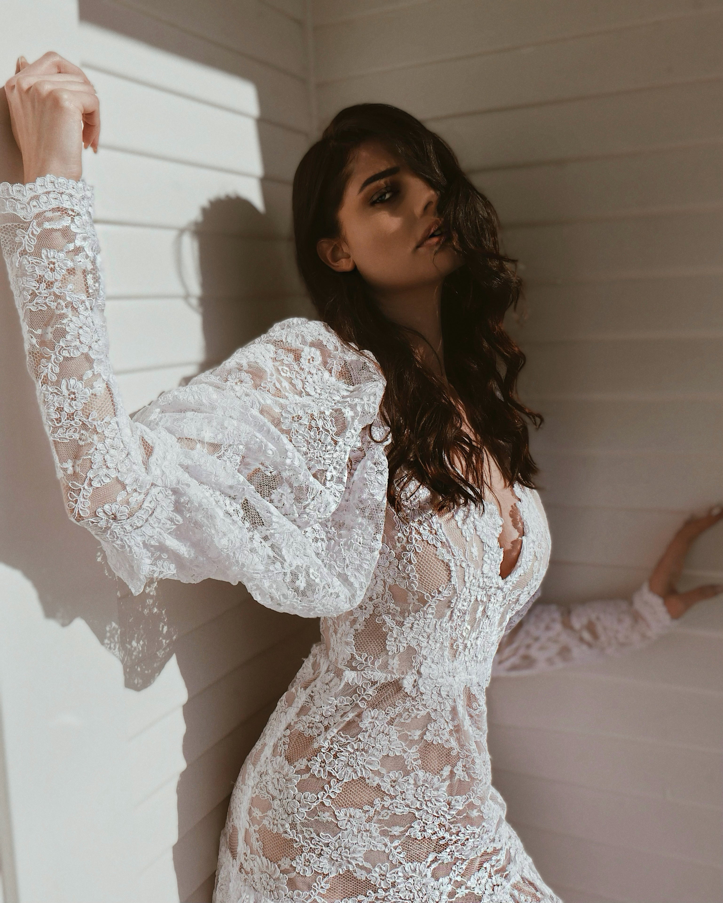 Side - A model poses in an oversized lace long sleeve wedding dress by Lauren Elaine.