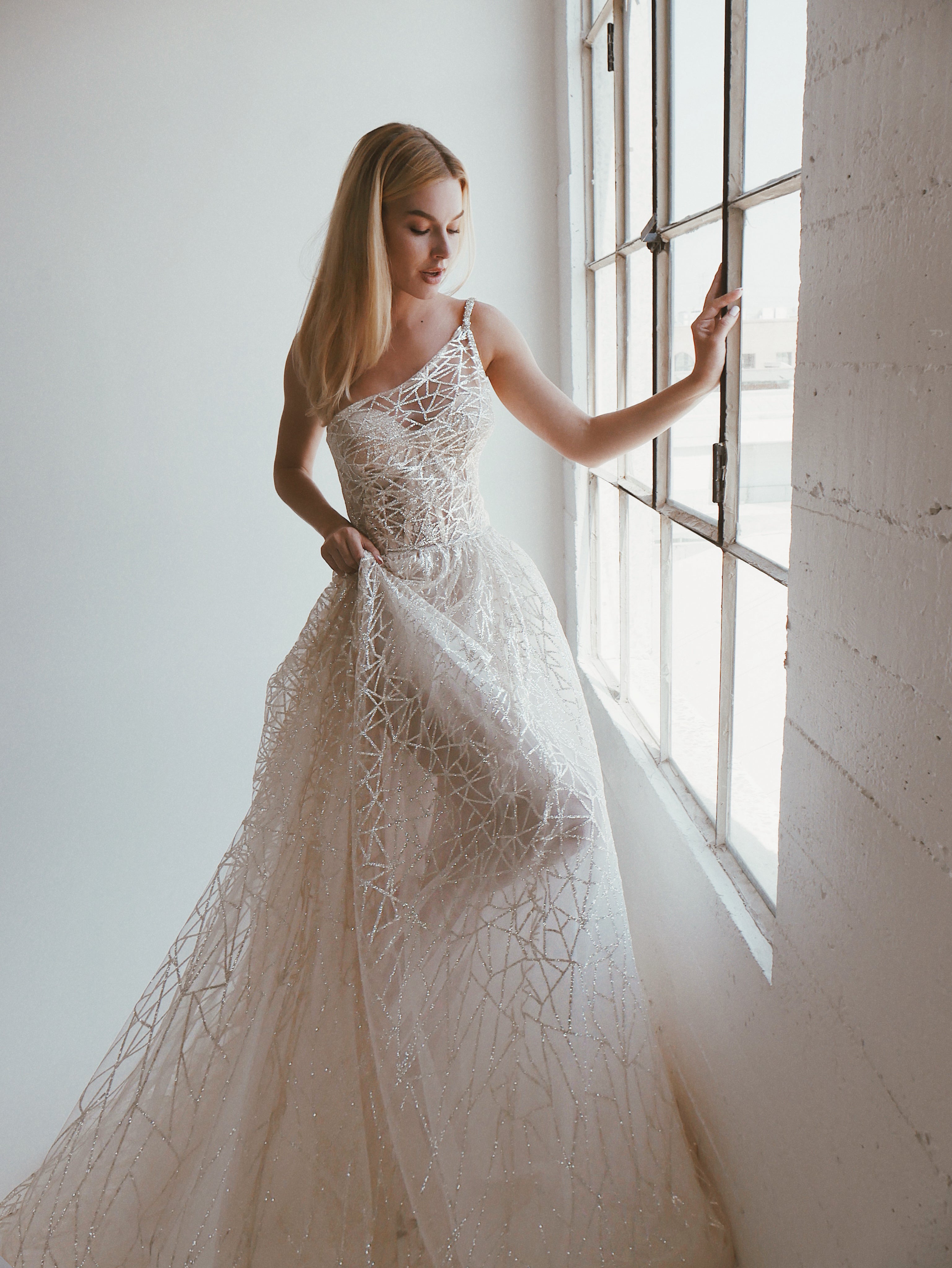 A model wears the Prima gown by Lauren Elaine Bridal featuring one shoulder corset with sparkle