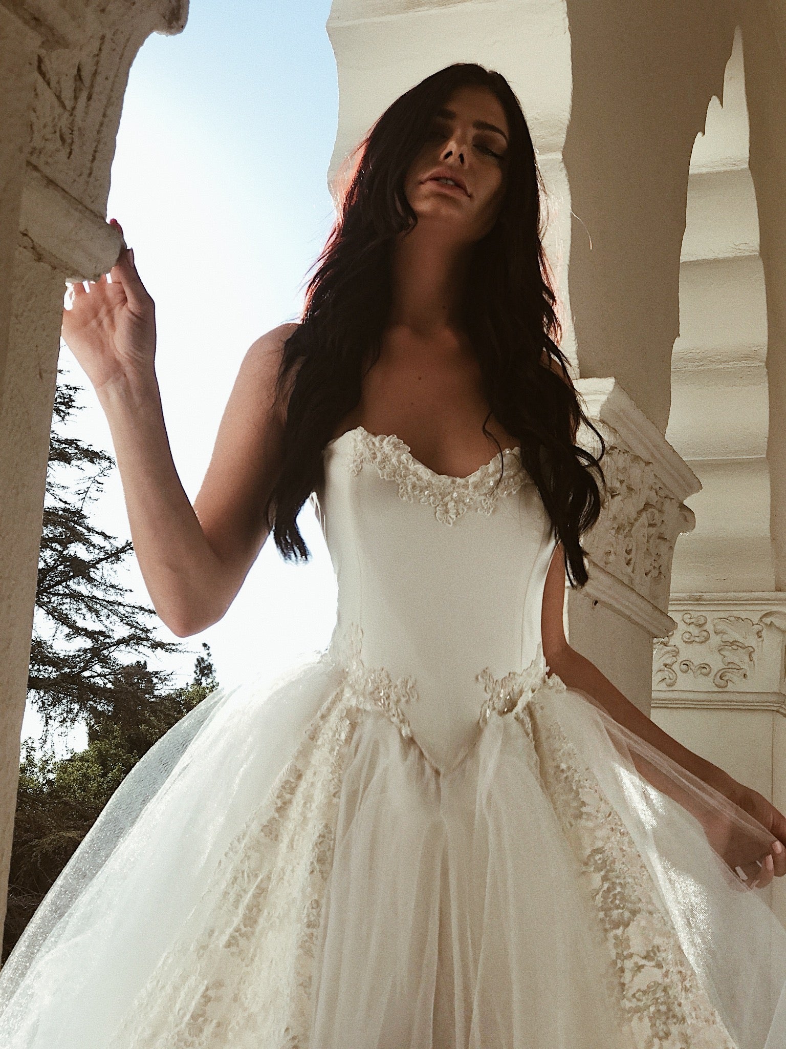 A model wears a tulle ball gown wedding dress with dramatic detachable cathedral train - closeup.