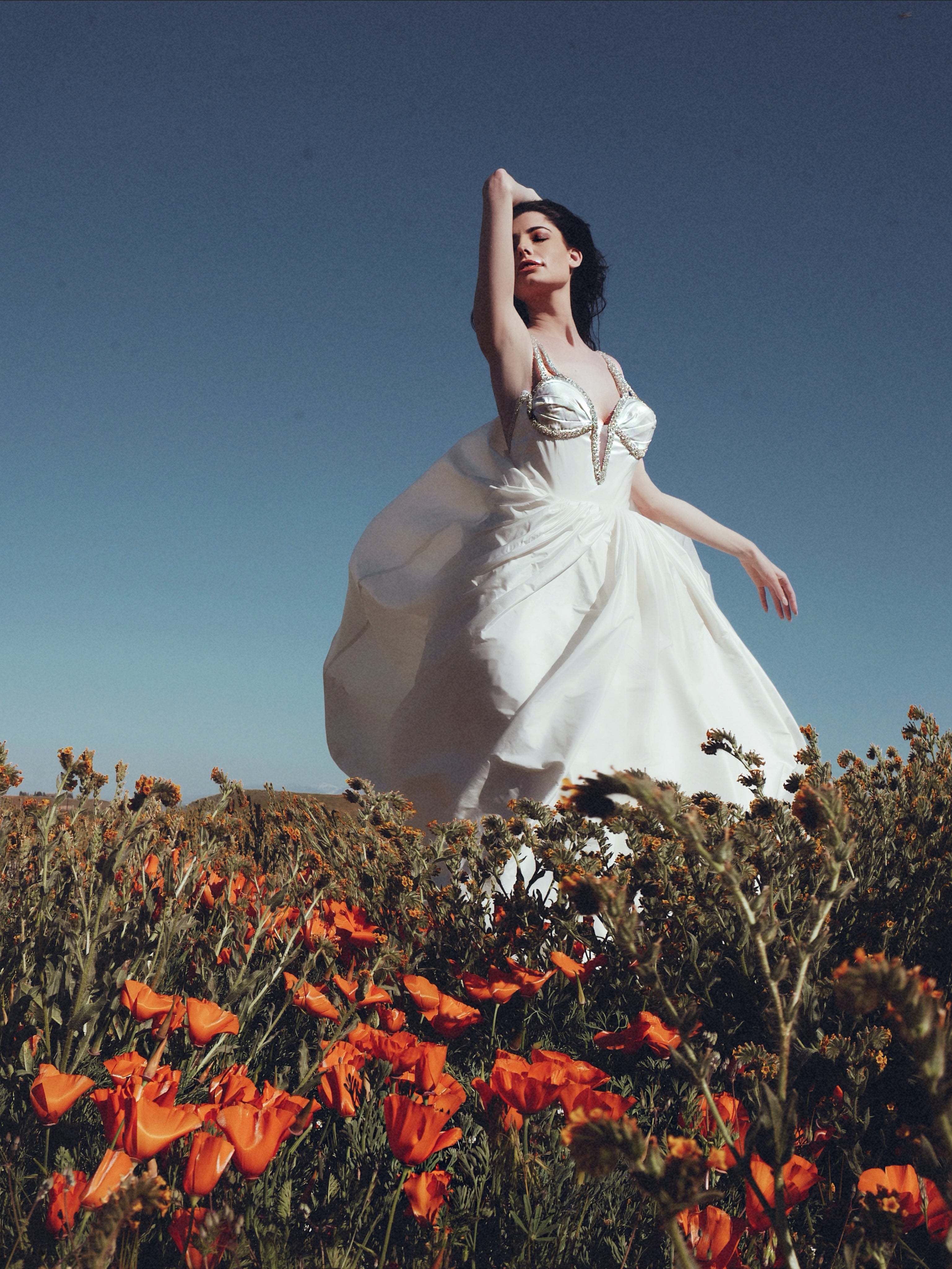 A model wears the Lauren Elaine Vespertine gown in a field of California poppies.