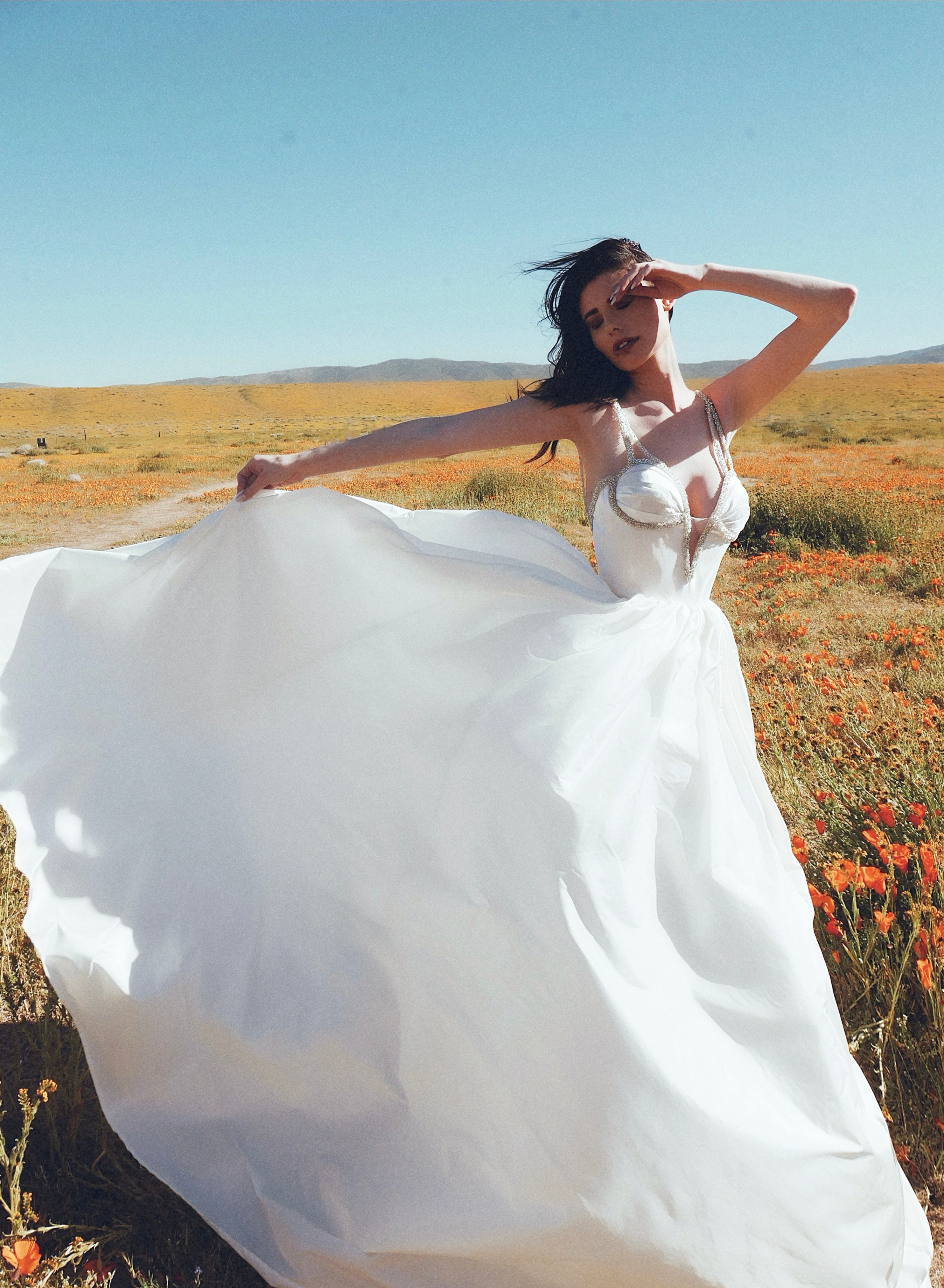 A model wears the Lauren Elaine Vespertine silk taffeta corset wedding dress in a field of poppies.