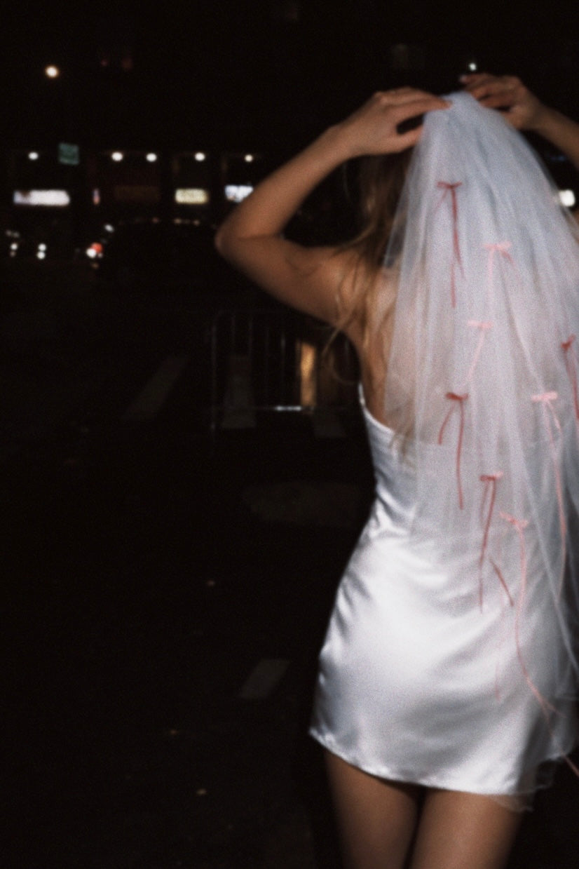 A bride wears a fingertip wedding veil with pink and red mini satin bows.