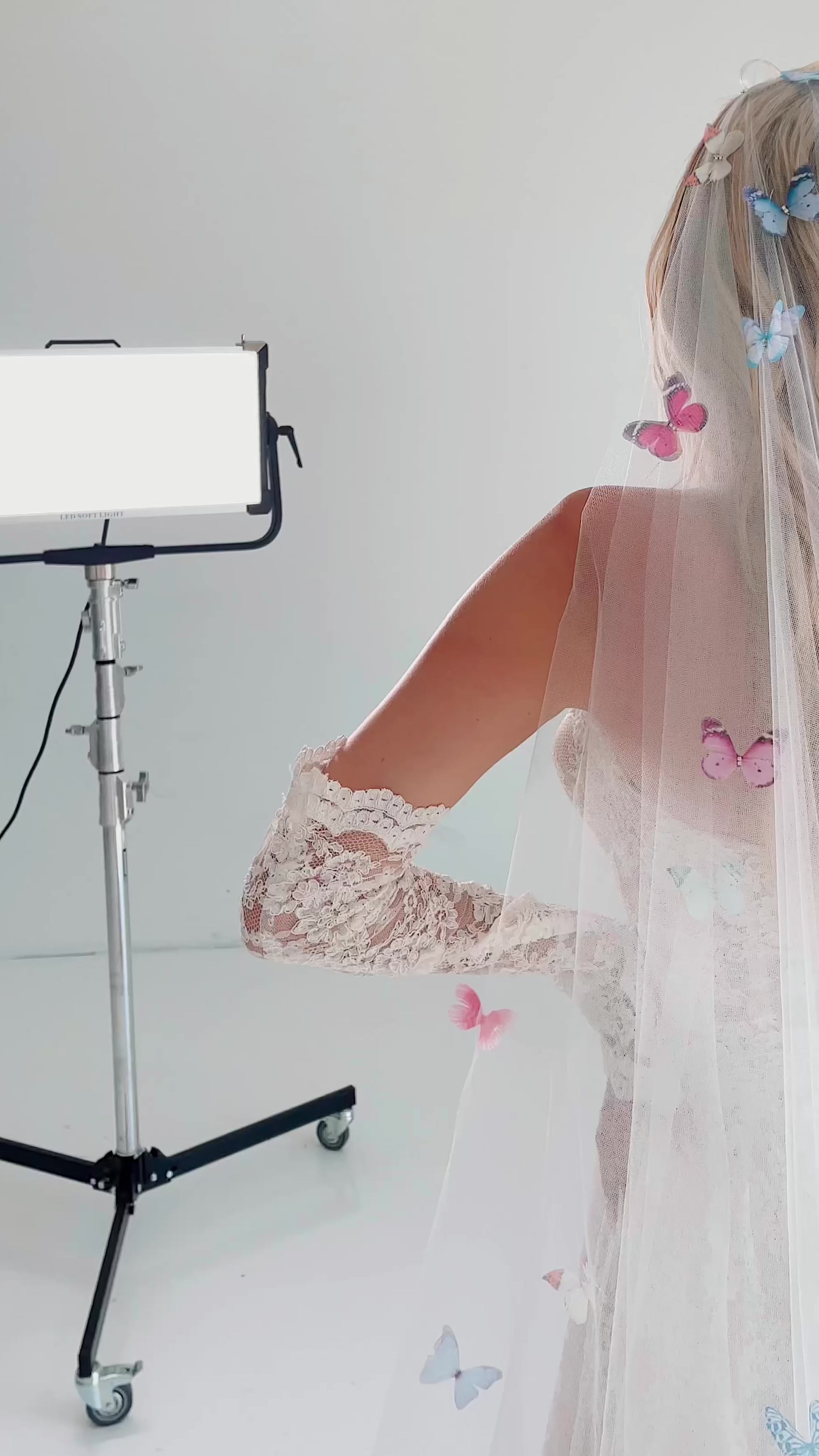 A model wears a rainbow butterfly wedding veil in a photo studio with the Lauren Elaine Kingsley Dress.