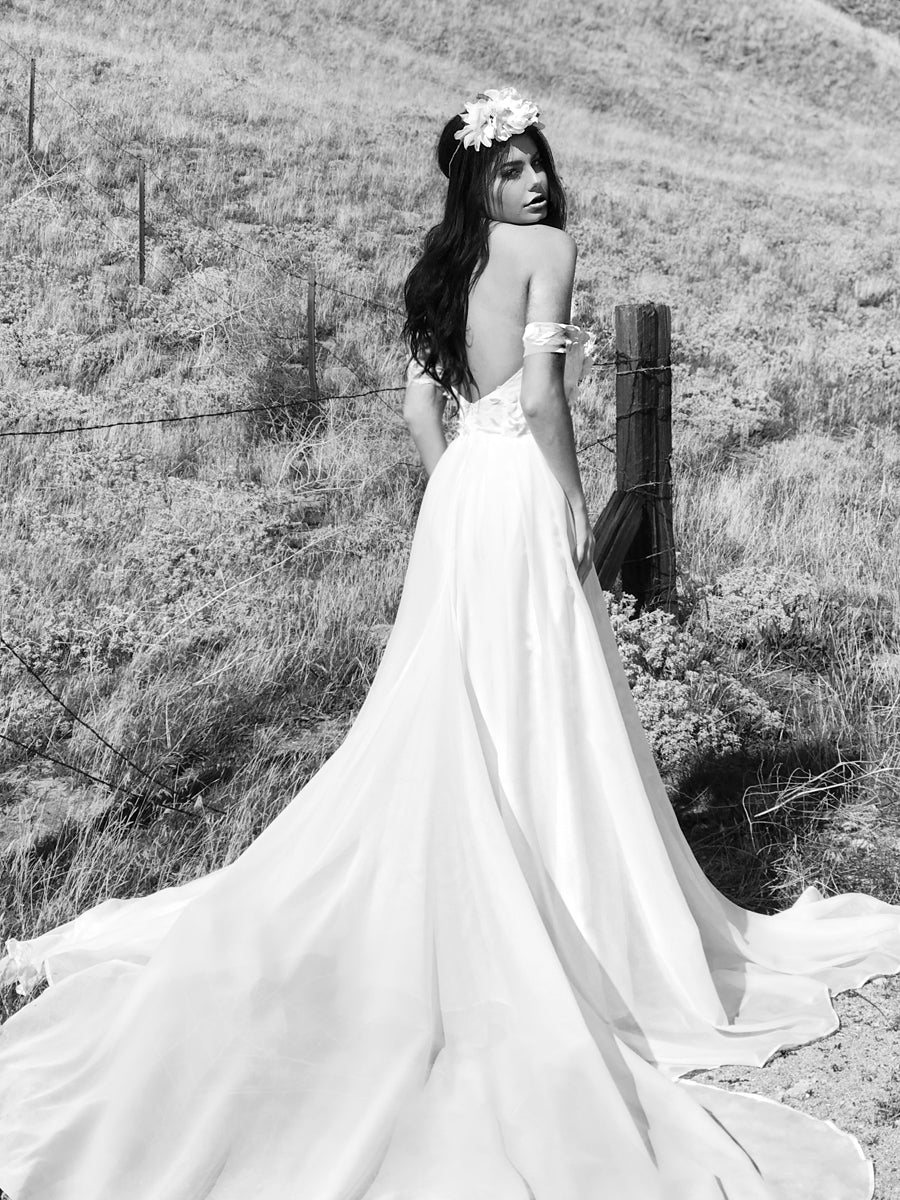 Romantic and bohemian off-the-shoulder wedding dress with lace floral appliques and sweeping cathedral train.